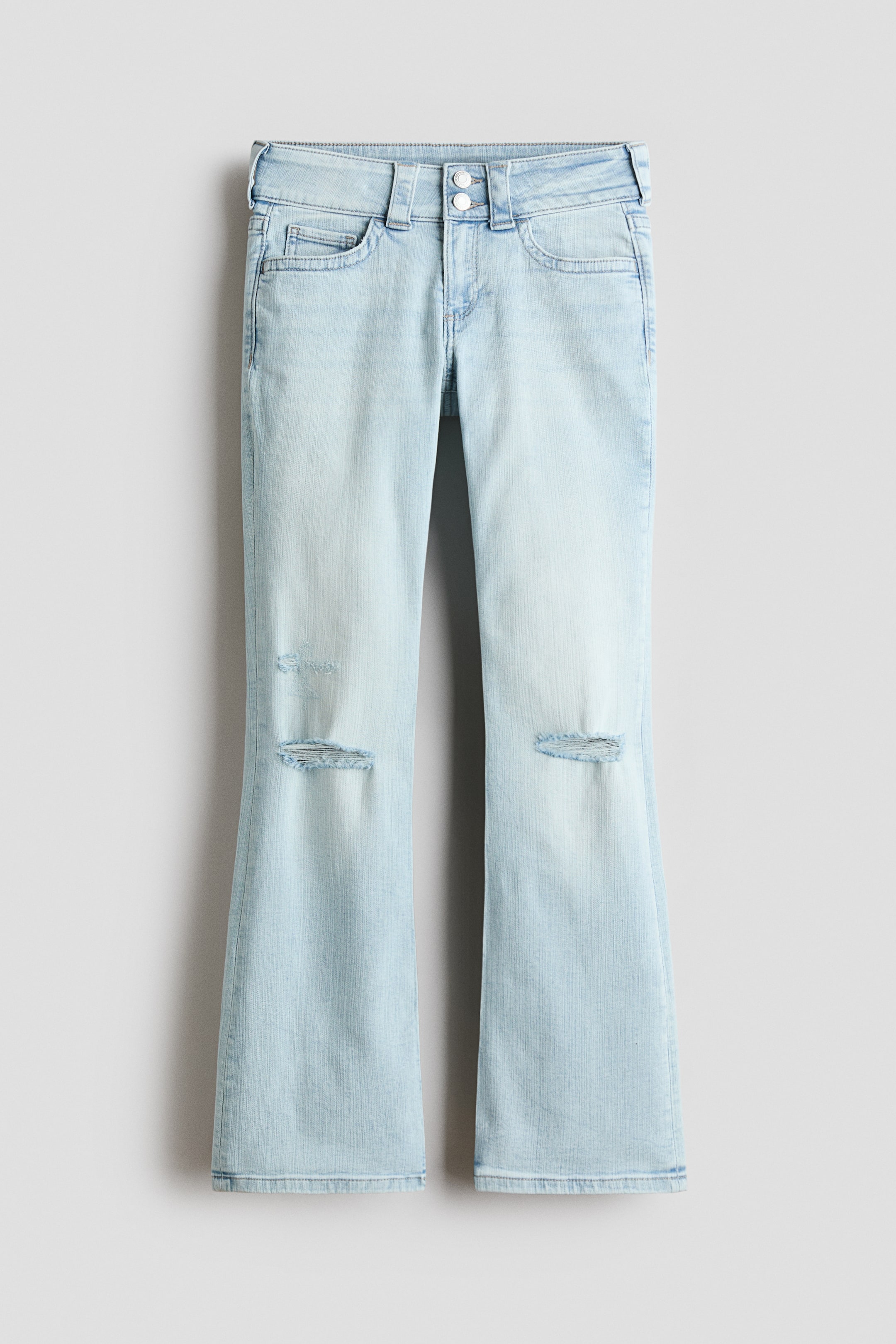 View larger image: Light blue washed denim bootcut jeans are showcased from the front, fitting slim from the waist to the thigh and flaring from the knee to the hem. They feature a low waist with a double button and zip fly fastening, and two distressed rips are visible on the front of each knee.
