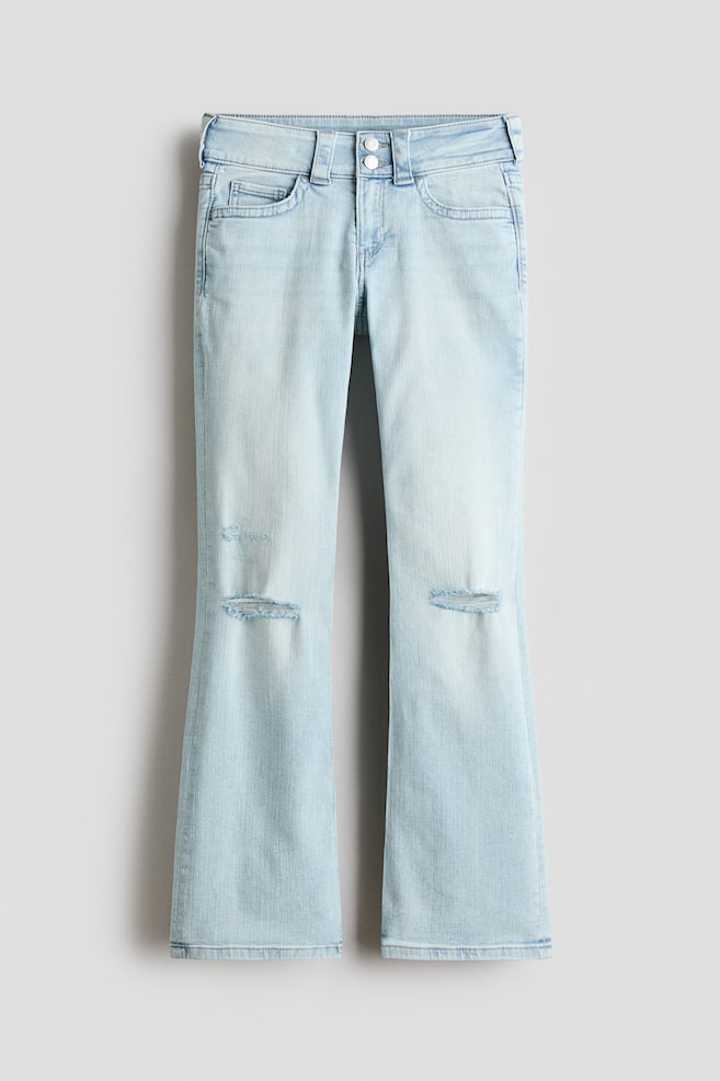 Light blue washed denim bootcut jeans are showcased from the front, fitting slim from the waist to the thigh and flaring from the knee to the hem. They feature a low waist with a double button and zip fly fastening, and two distressed rips are visible on the front of each knee. - 1