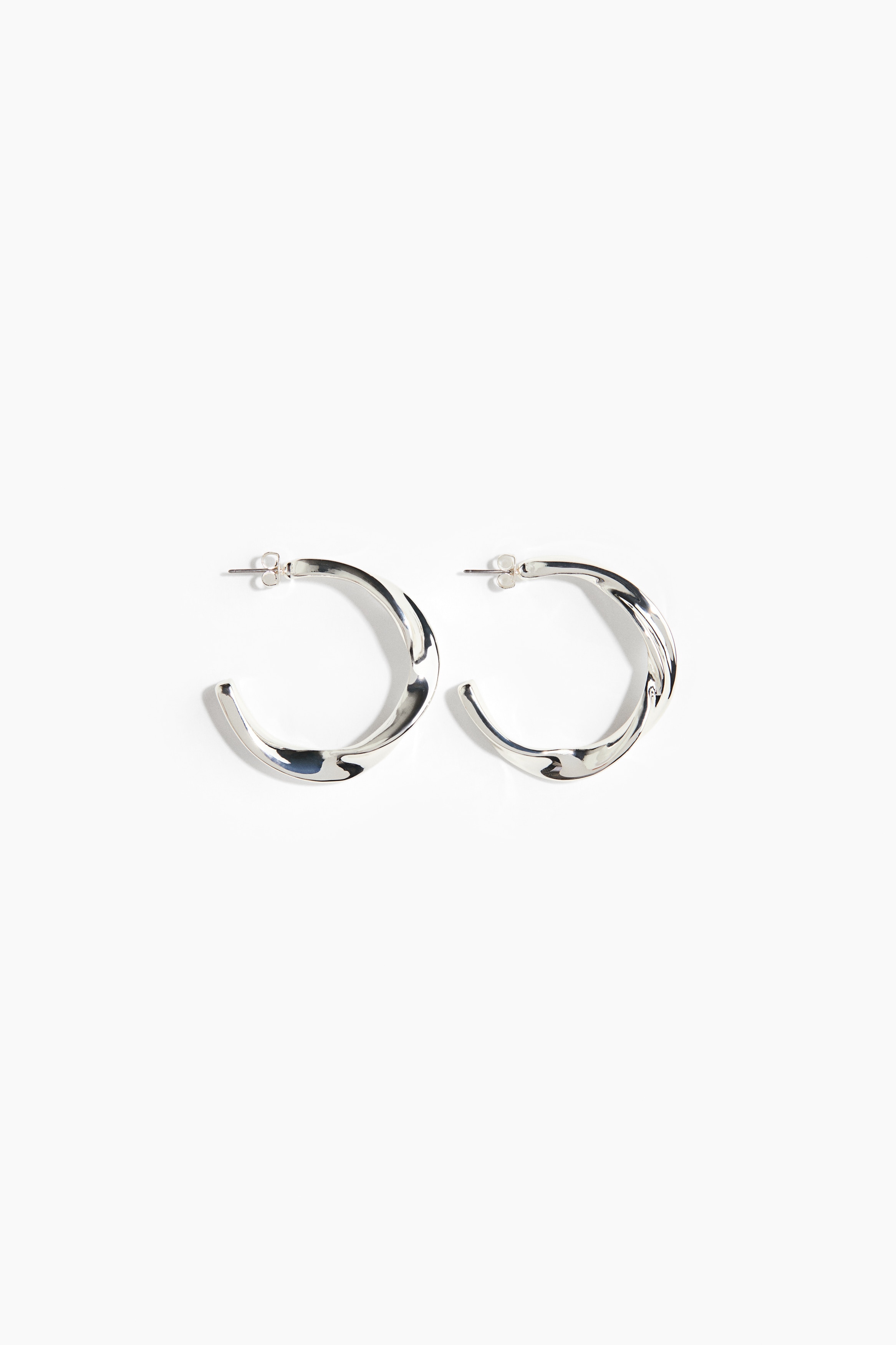 Ãredobber i sÃ¸lvfarget metall med ringform og et kraftig, tvunnet design bÃ¦res pÃ¥ modellens Ã¸re i sideprofil.