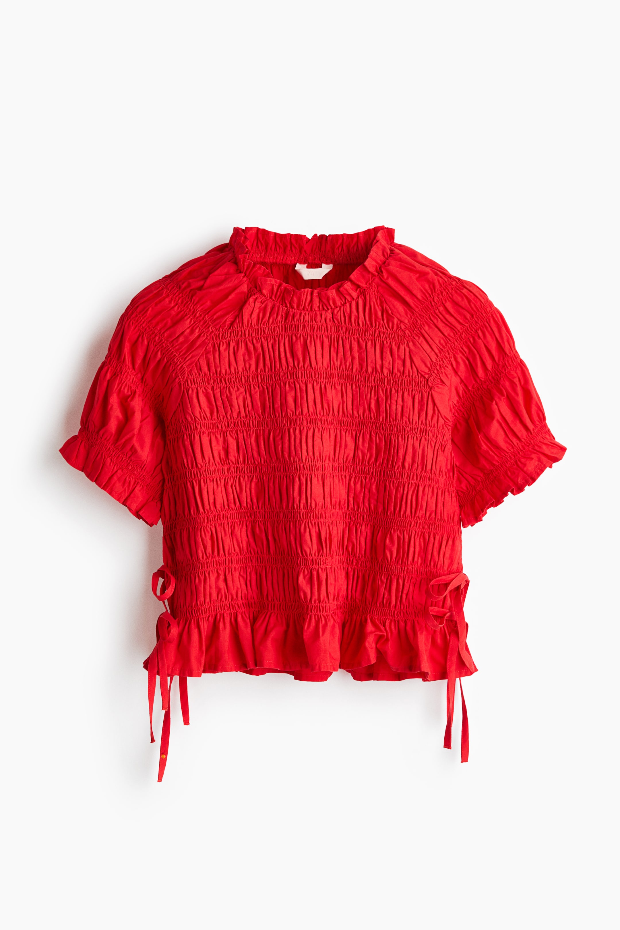 View larger image: A red top showcasing an extensively shirred body and short puffed sleeves, front-facing. It is crafted with a ruffled high neck and a ruffled hem, featuring decorative side ties.