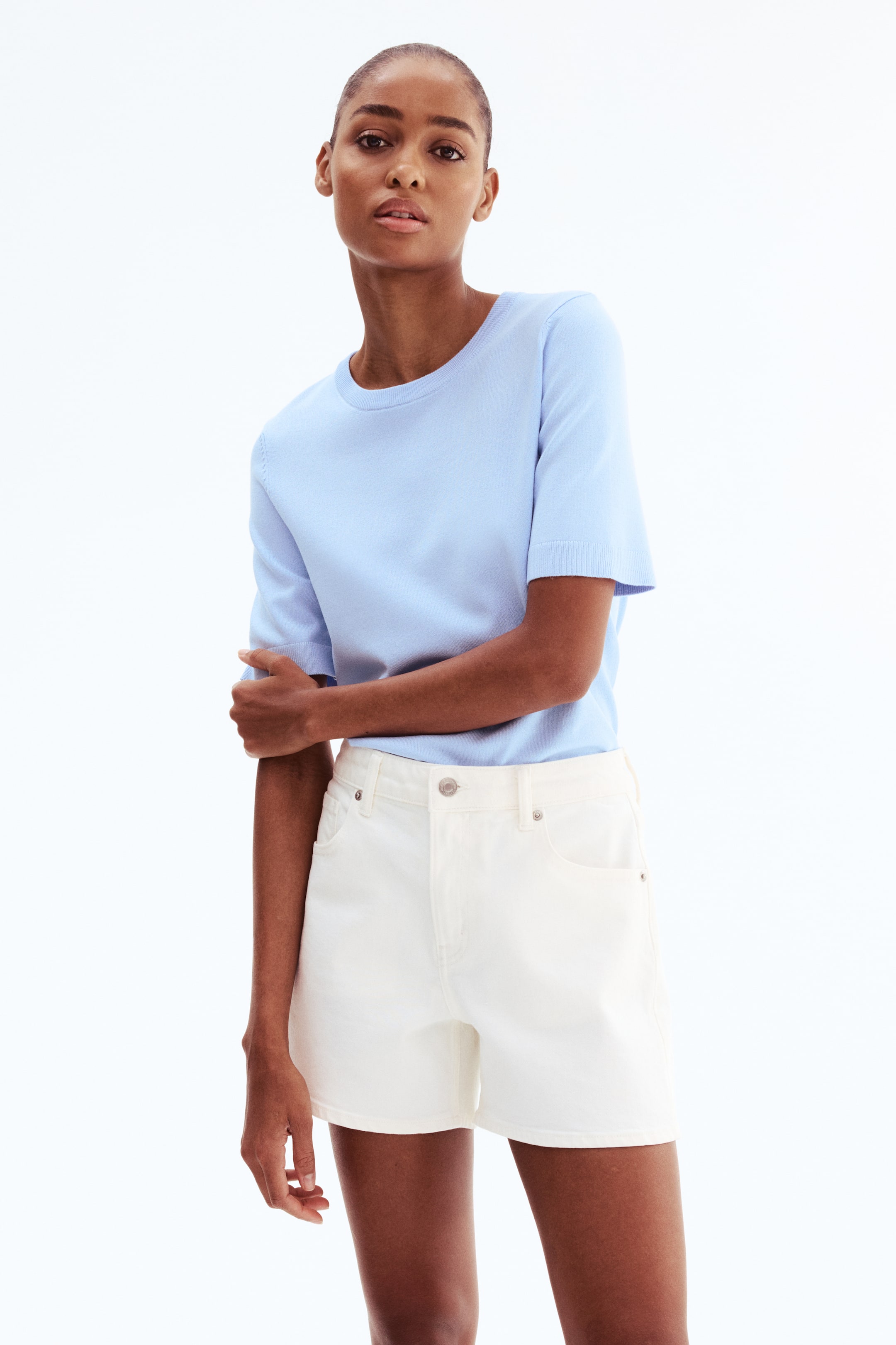 View larger image: The model is wearing white 5-pocket cotton denim shorts. They feature a regular waist, a button-and-zip fly closure, and visible front and coin pockets.