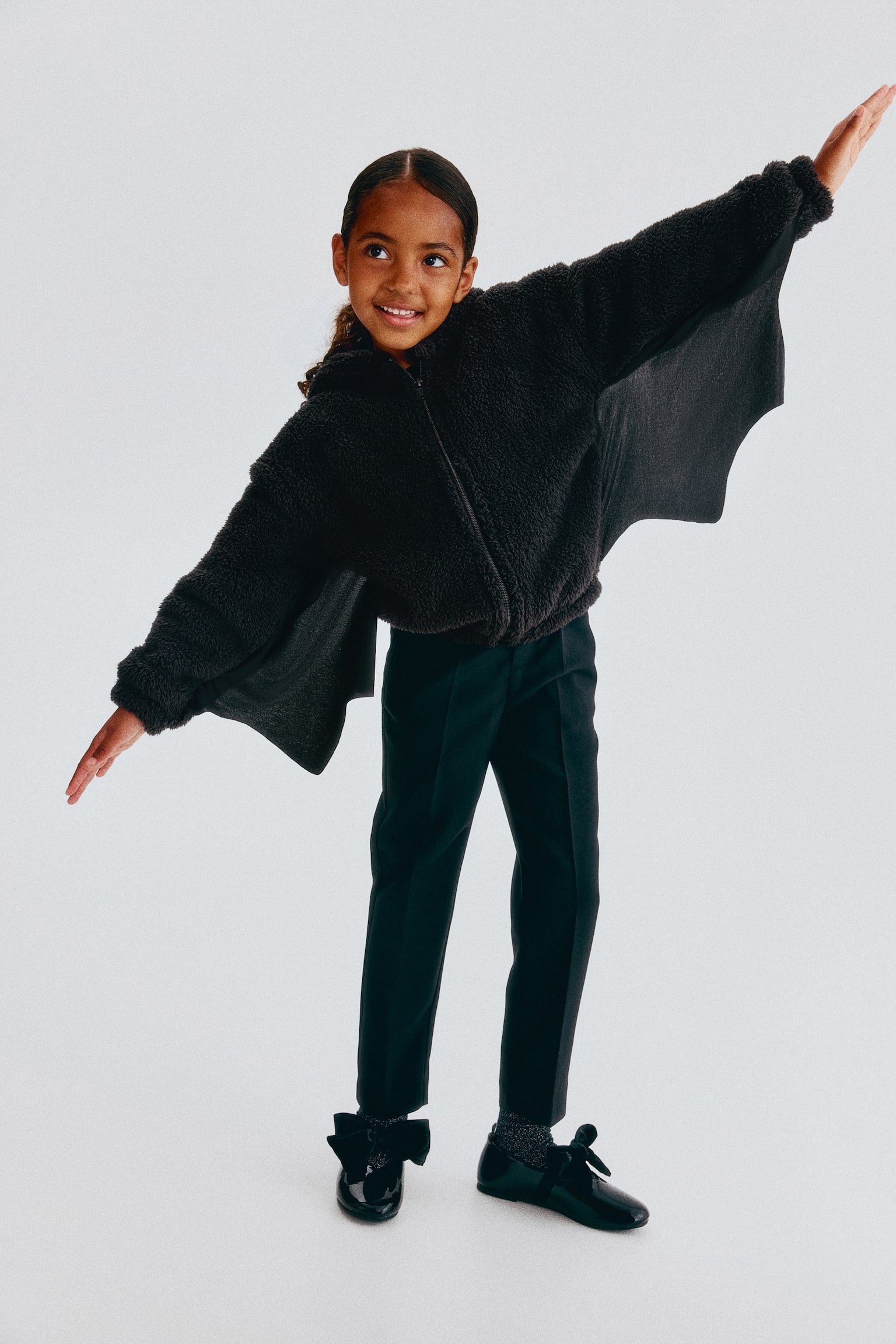 A black teddy fleece jacket is facing forward. Its hood is detailed with pointed ears, white eyes with black pupils, and two white fangs. A full-zip closure runs down the centre front. - 1