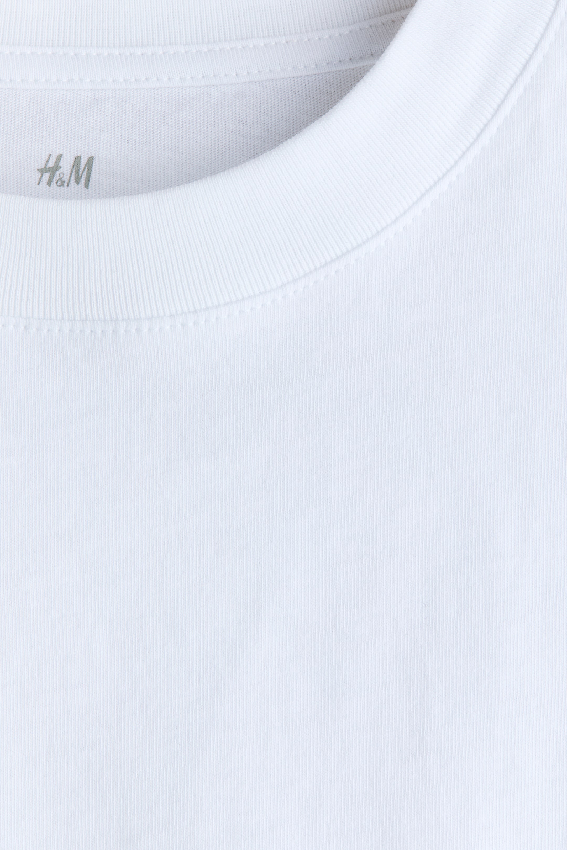 Se større billede: Den hvide t-shirt har en ribbet rund halsudskæring, med H&M-logoet synligt på indersiden af nakken, præsenteret fra forsiden. Hoveddelen af trøjen viser en glat jerseystrik tekstur.