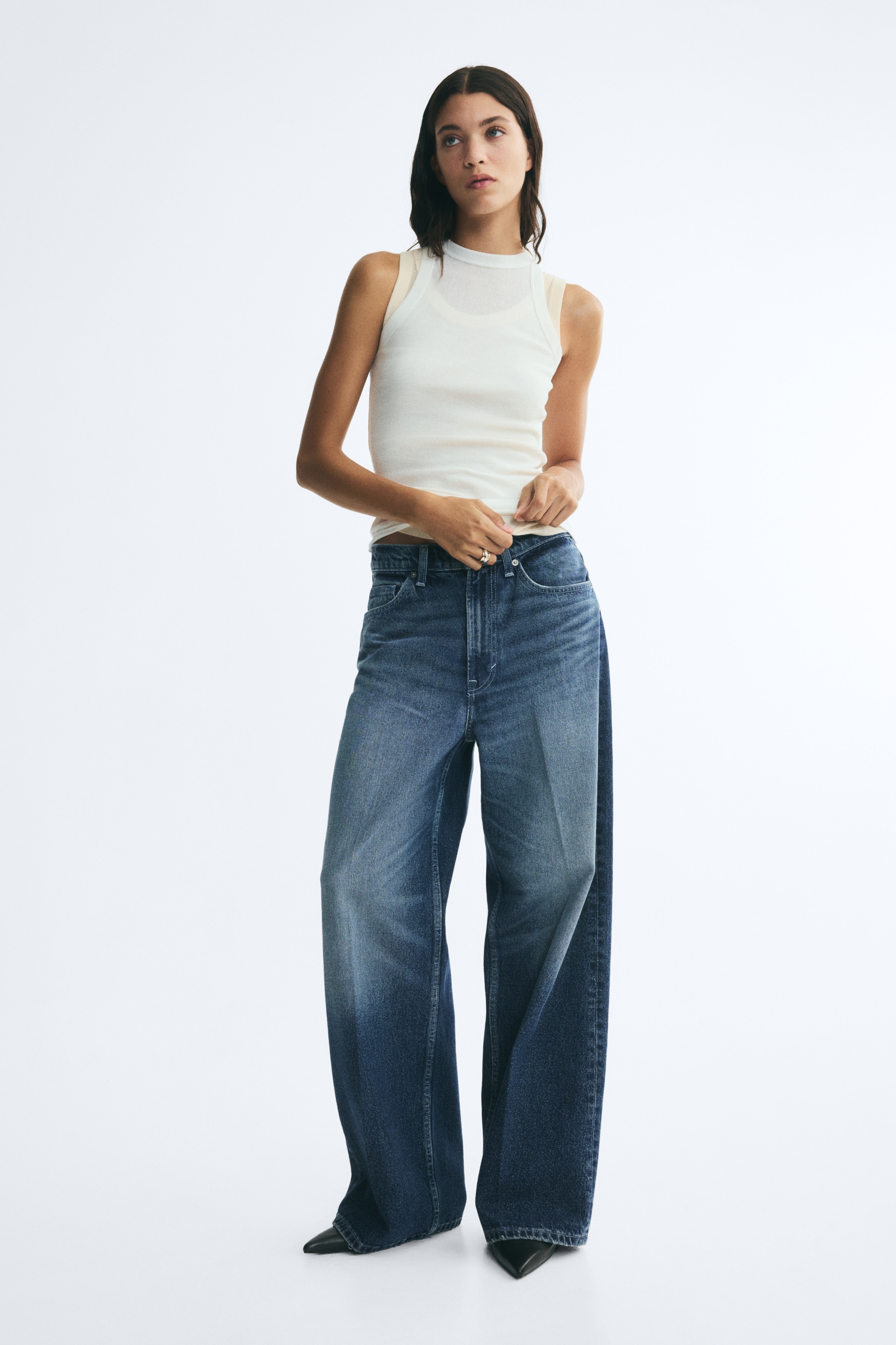 These blue denim jeans are shown from the front, featuring a loose, wide-leg fit with sharp pressed creases running down the centre of each leg. The jeans feature a faded, whiskered wash across the lap and thighs, a classic five-pocket construction, and a regular waist with a button fastening.