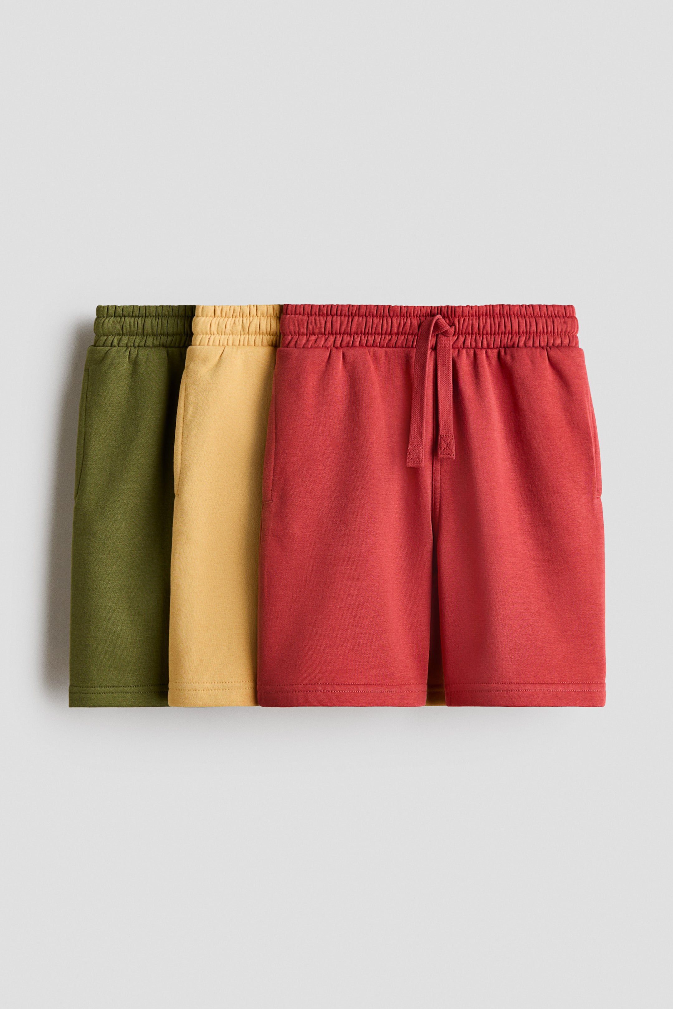 View larger image: Three pairs of shorts, crafted from lightweight sweatshirt fabric, come with an elasticated, drawstring waist and subtle side pockets. They are displayed in olive green, mustard yellow, and red, with the foremost red pair clearly visible from the front.