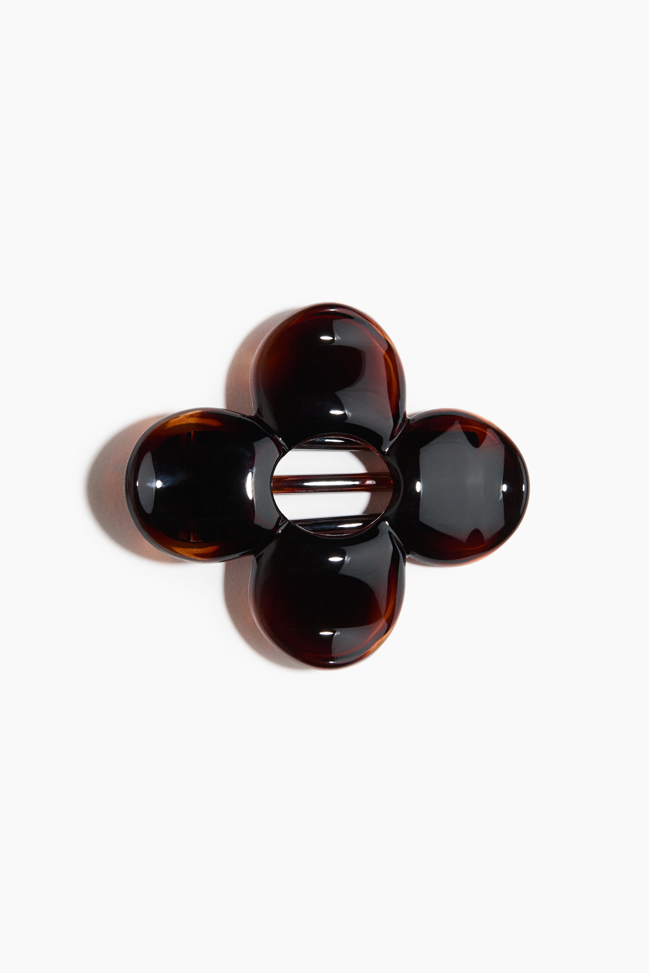 Voir une image plus grande: Une pince à cheveux en écaille de tortue présente un design en forme de fleur avec quatre pétales arrondis et brillants, vue de dessus. Son ouverture ovale centrale révèle deux barres horizontales du mécanisme de la pince.