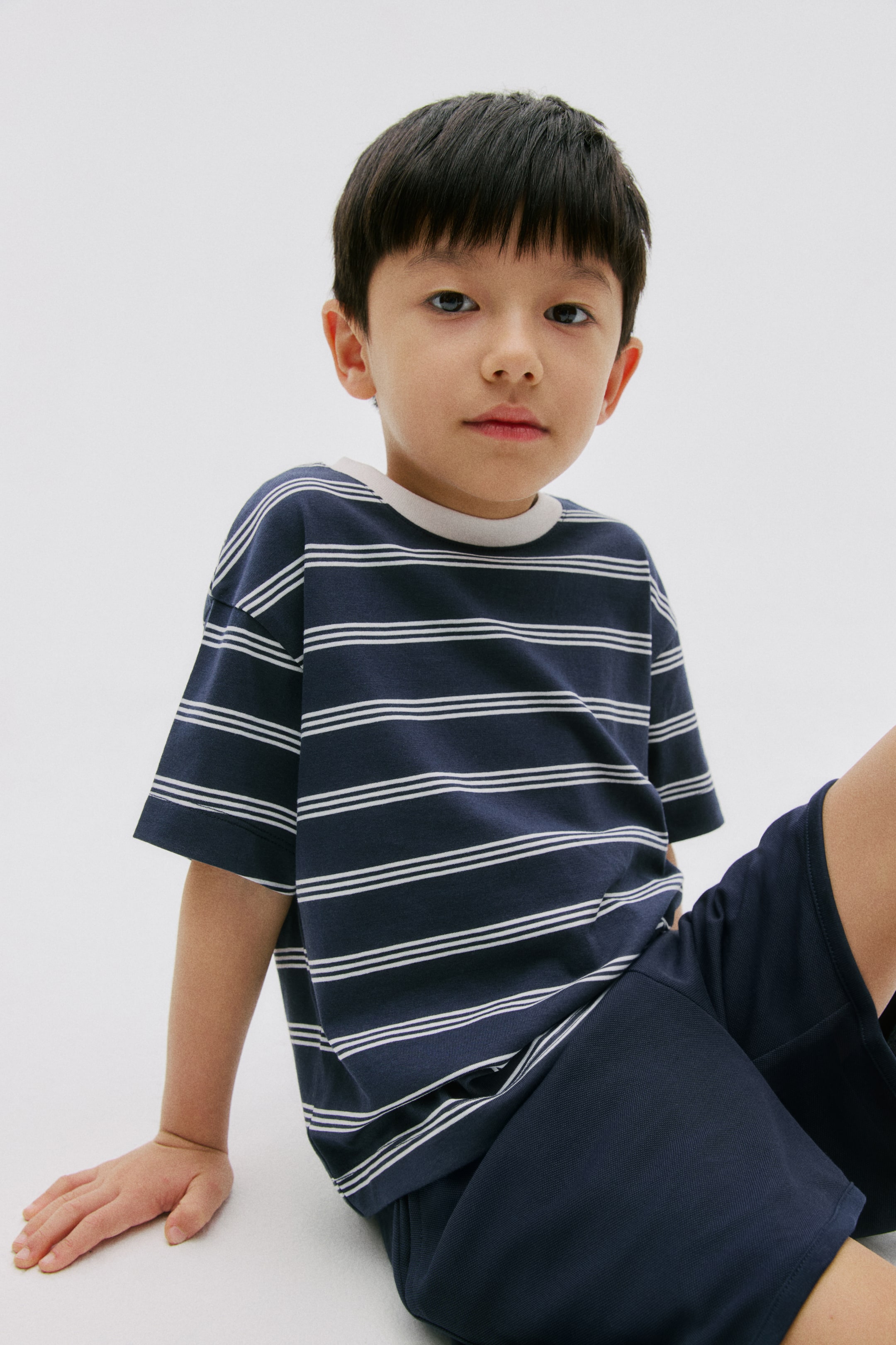 View larger image: A navy blue t-shirt is displaying multiple thin white horizontal stripes, a light-colored ribbed crew neck, and short sleeves. It is being paired with solid navy blue shorts.
