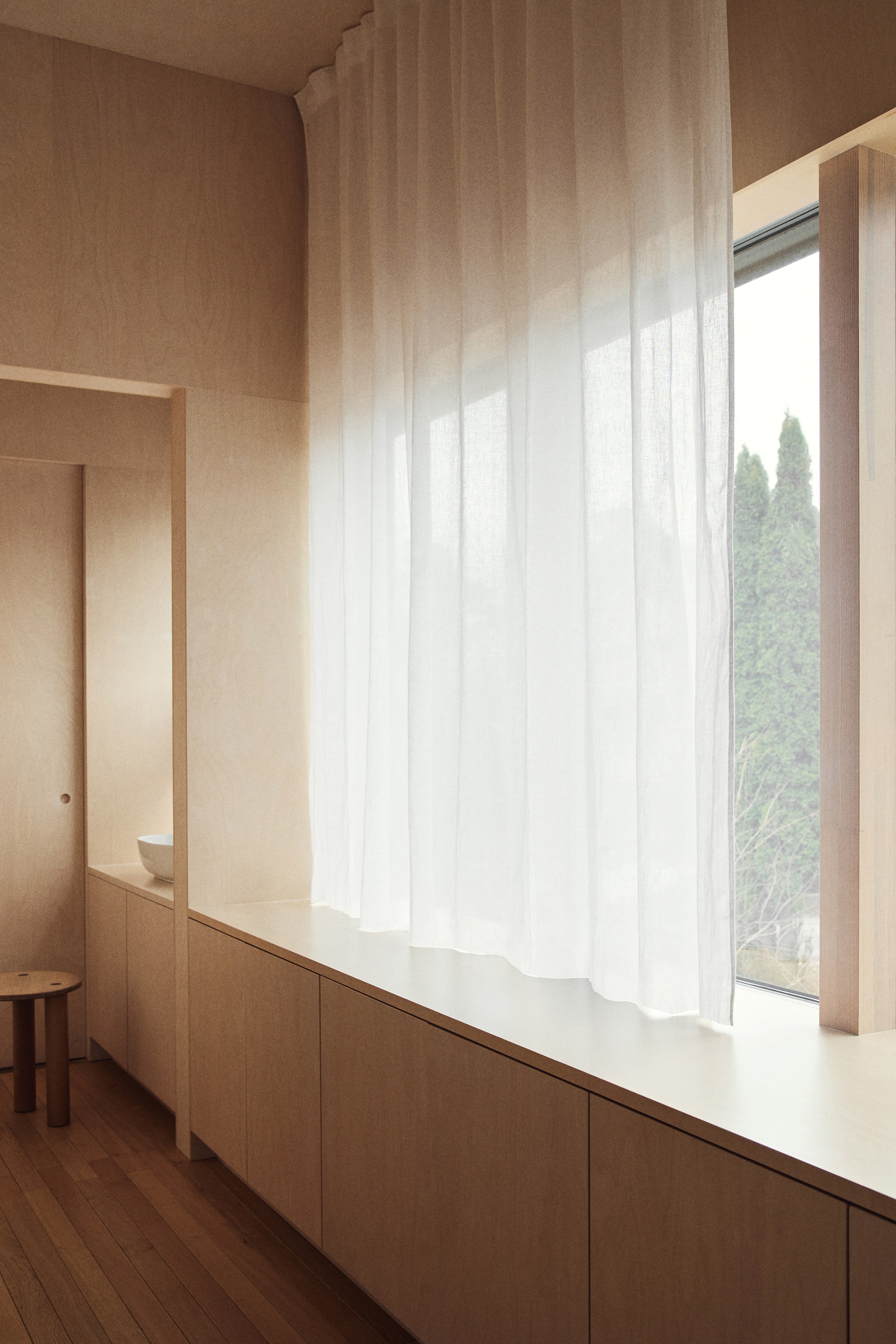 Vis større bilde: En skjær hvit gardin henger, dekker et vindu og danner myke vertikale folder av gjennomsiktig stoff.
