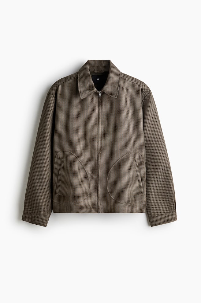 Eine braun-beige Hahnentrittjacke wird von vorne präsentiert, mit einem durchgehenden Reißverschluss und einem spitzen Kragen. Sie ist mit zwei großen, geschwungenen Taschen mit gestickten Umrissen auf der unteren Vorderseite und langen Ärmeln mit geraden Manschetten gestaltet. - 1
