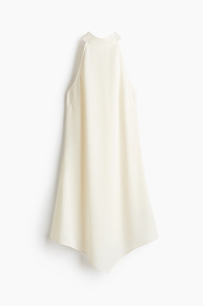 An off-white halter top is hanging, displaying a high neck that forms a standing collar at the back. It is featuring a loose, flowing silhouette and is finished with an asymmetrical hemline creating soft points at the sides. - 1