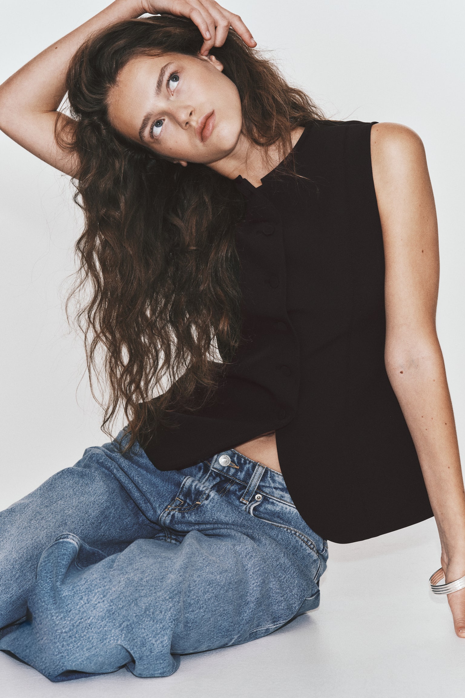 A black sleeveless waistcoat is shown from the front, featuring a round neckline and a full button placket with six matching black buttons. The waistcoat is designed with tailored vertical seams on the front and a subtly curved hem. - 1