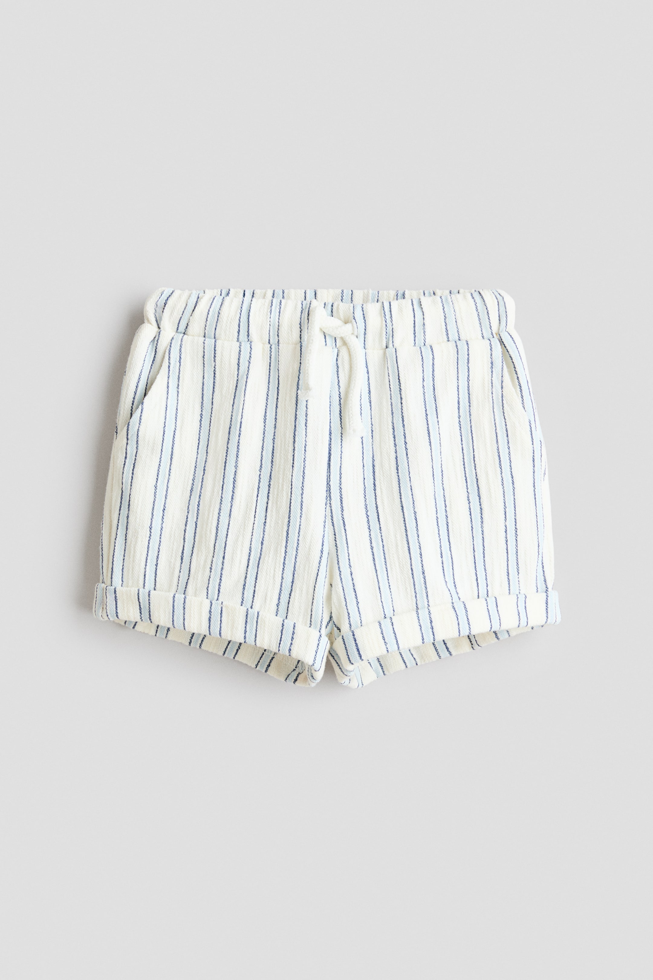 View larger image: The shorts are shown from a front perspective, featuring an off-white textured fabric with vertical stripes in dark blue and light blue. Designed with an elasticated waistband, a white drawstring tie, side pockets, and cuffed hems.