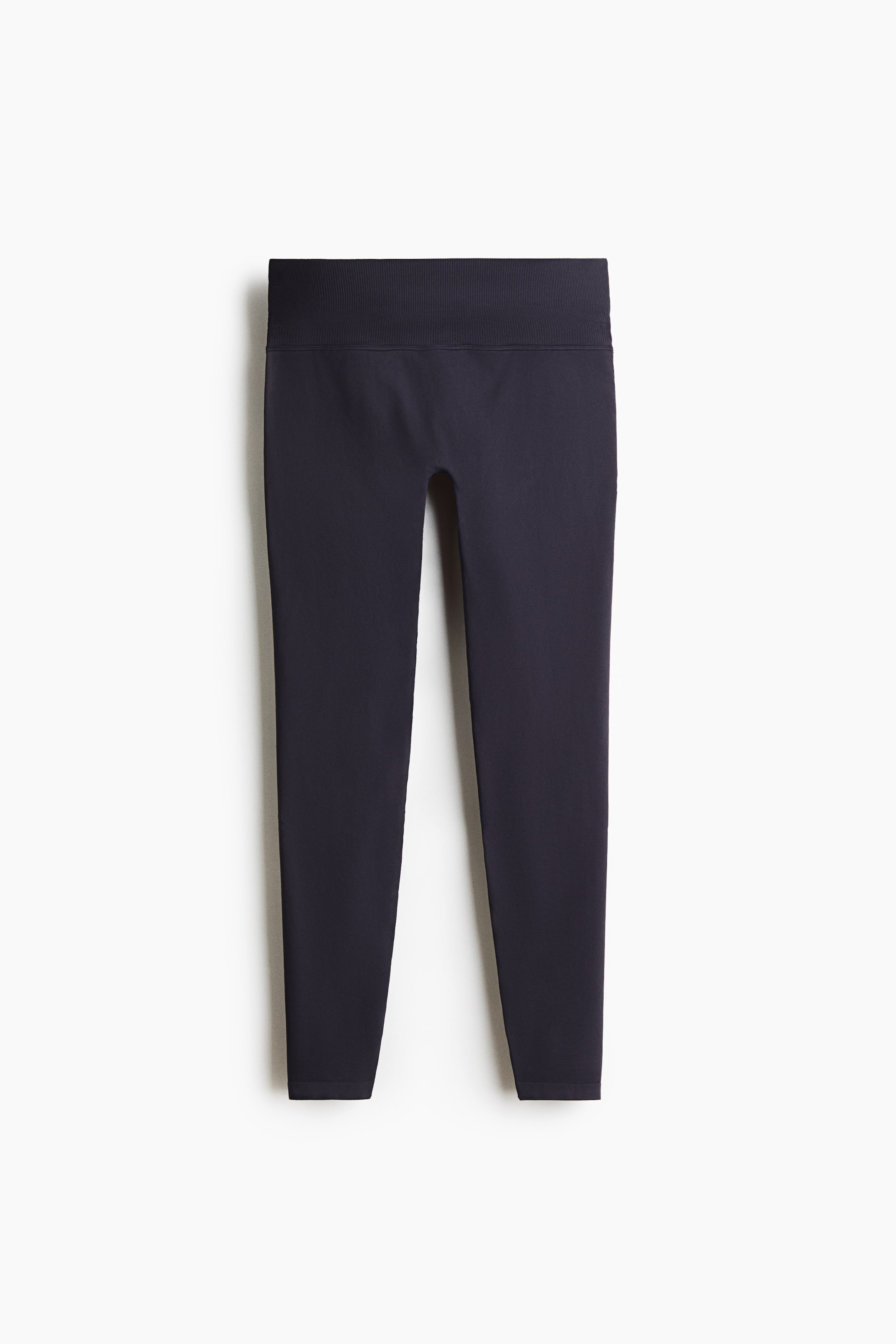 Ampliar la imagen: Un par de leggings gris oscuro está de frente, mostrando una pretina acanalada alta y ancha, y un diseño ceñido y sin costuras que se ajusta hasta los tobillos.