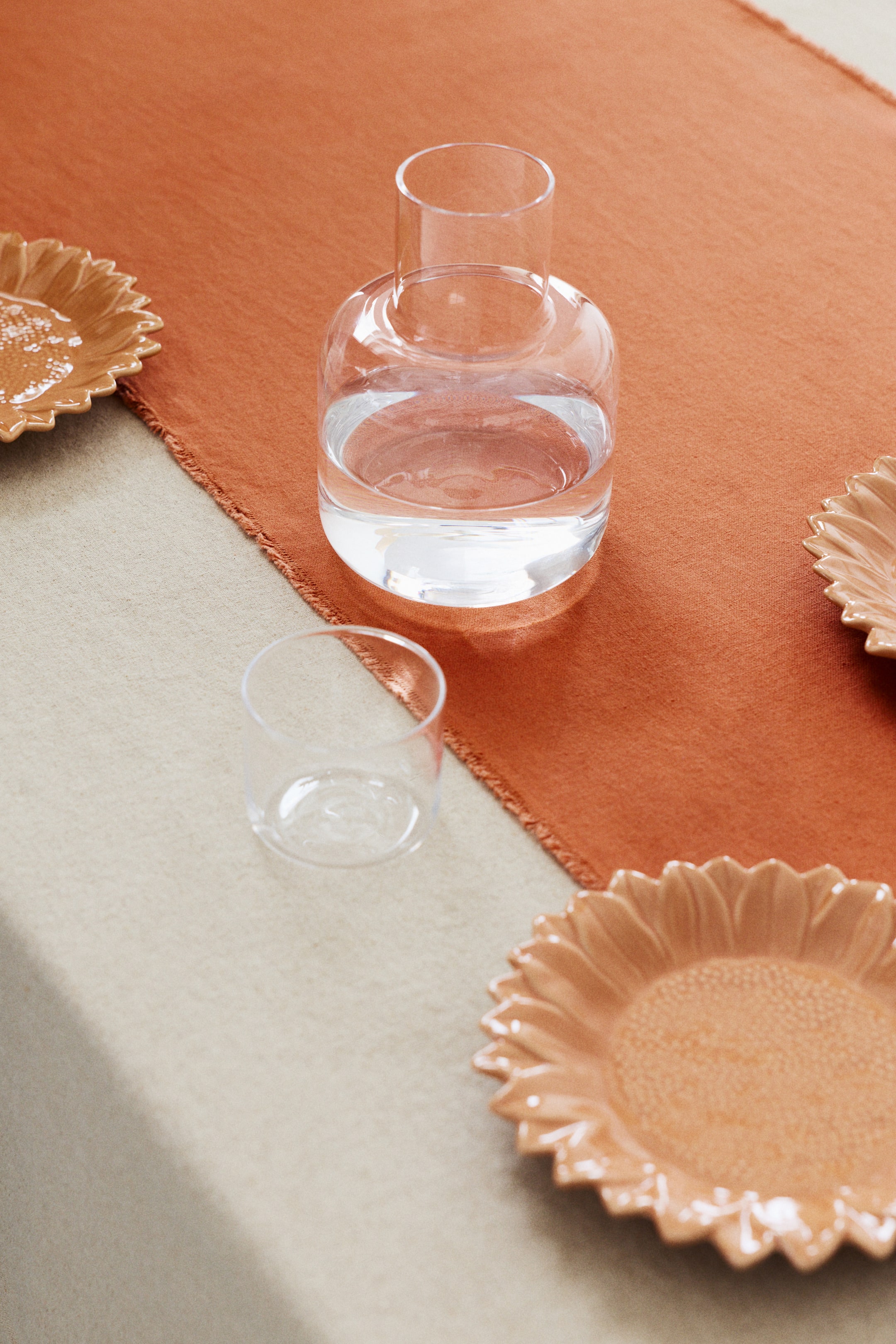 Vis større bilde: En klar glasskaraff med en rund kropp og en høy, smal sylindrisk hals, fylt med klart vann, presentert fra en litt forhøyet, forovervendt vinkel.