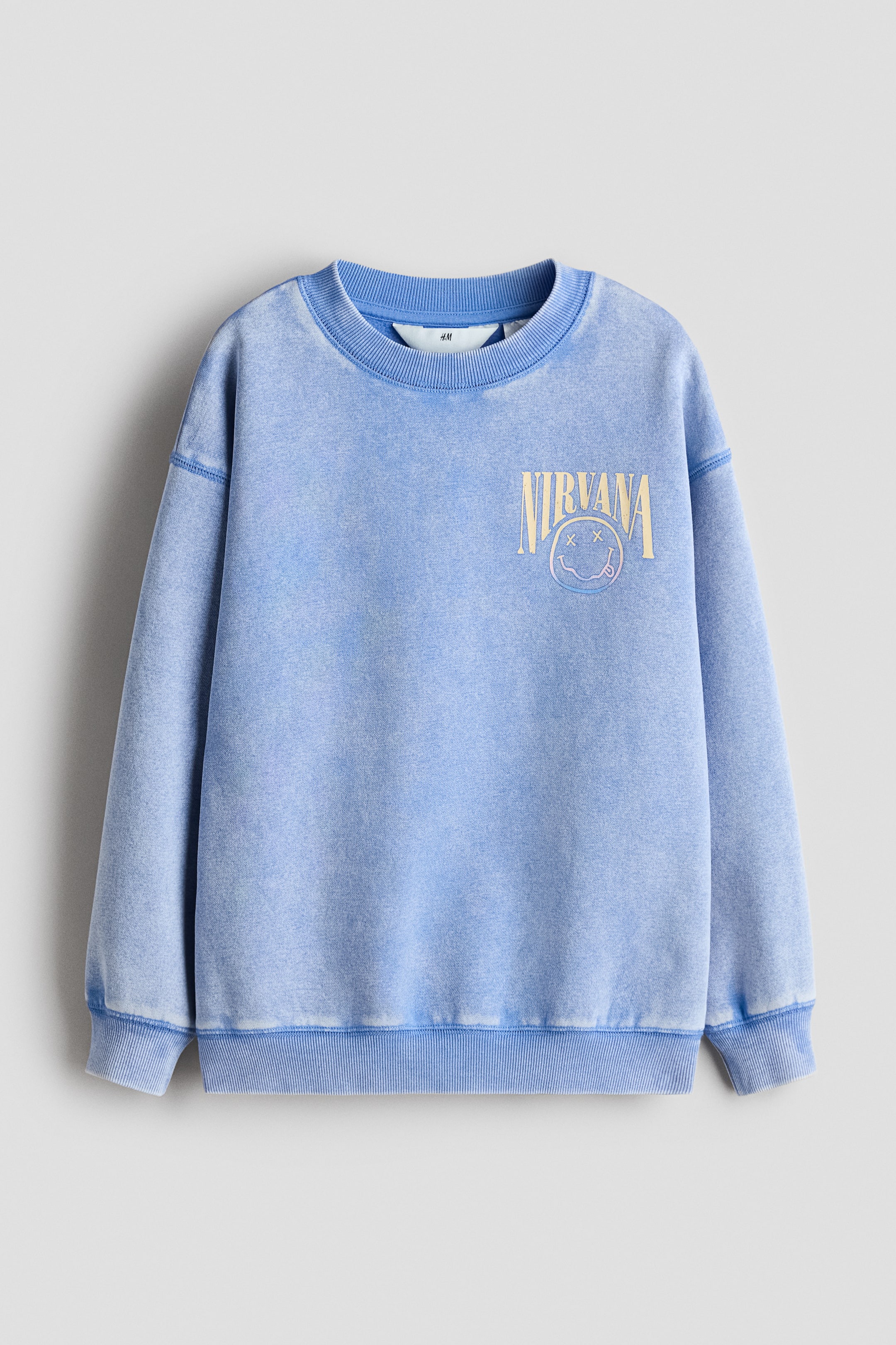View larger image: Front-facing oversized blue sweatshirt featuring a washed effect with a 'Nirvana' text and smiley face logo print on the chest. Designed with a round, rib-trimmed neckline, dropped shoulders, and ribbing at the cuffs and hem.