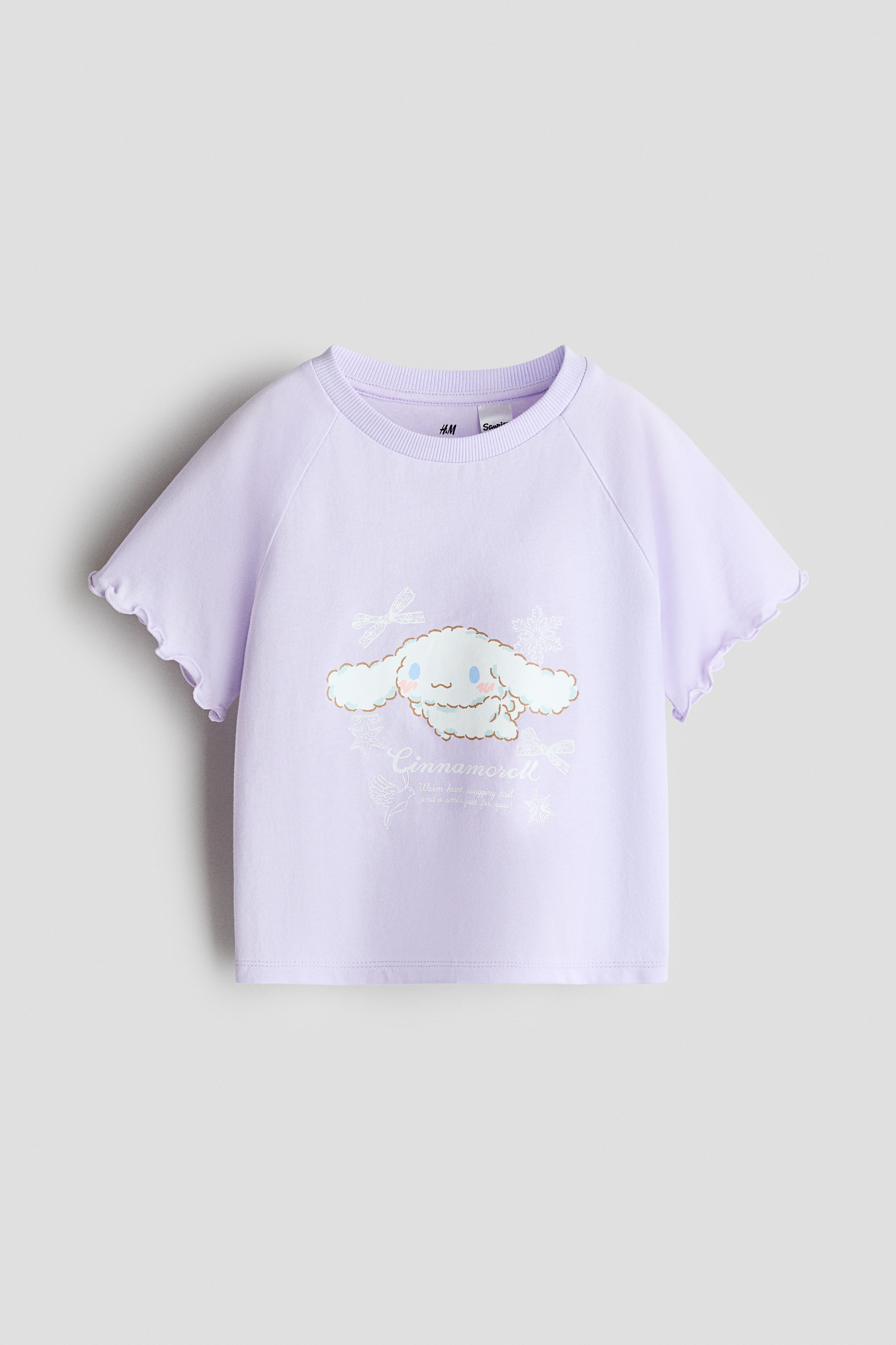 The model is wearing a light purple cotton jersey T-shirt featuring a printed cartoon character on the front. The T-shirt has a round rib-trimmed neckline, short raglan sleeves with overlocked edges and a straight hem, and is paired with wide-leg ombrÃ© denim jeans.