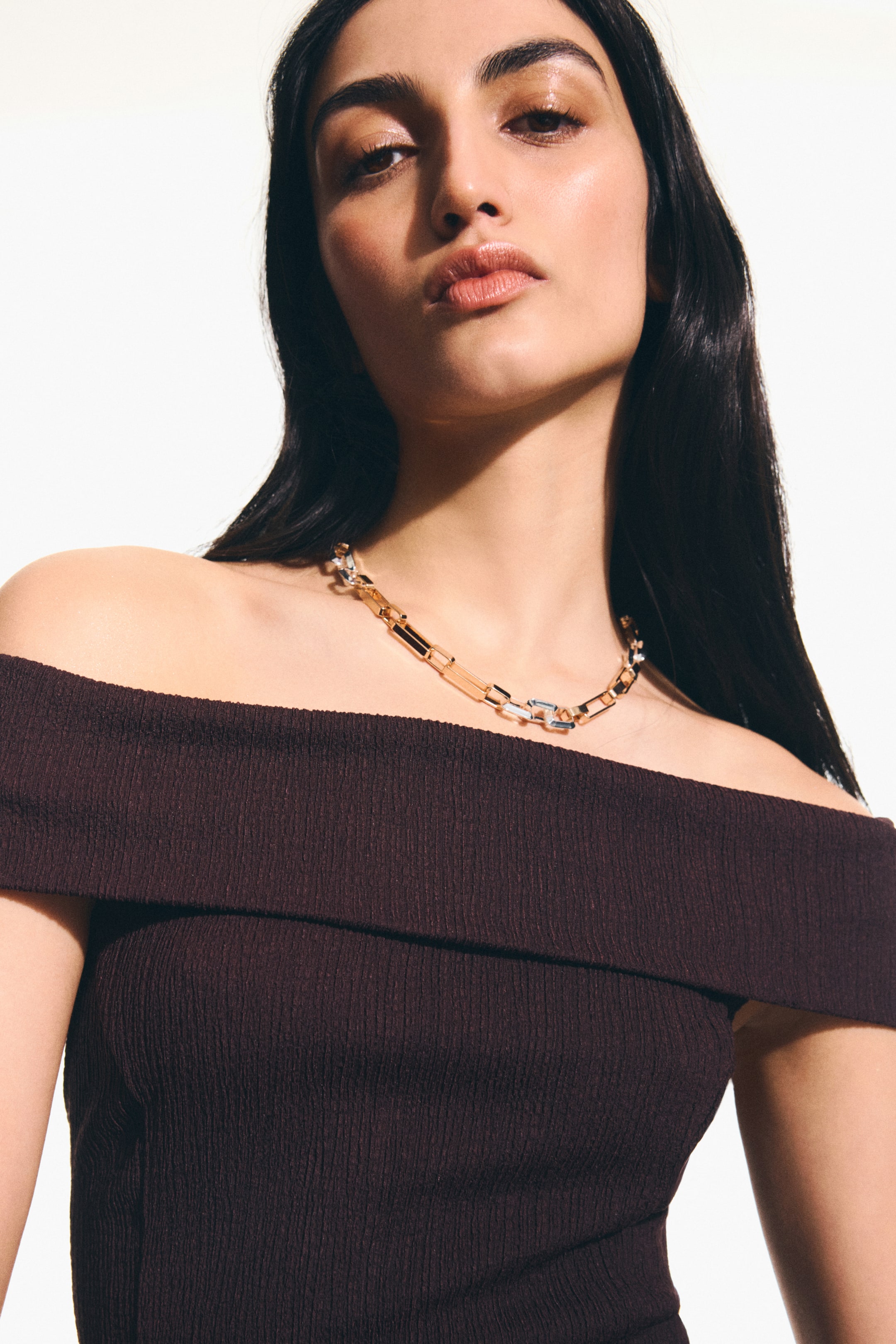 Преглед на по-голямо изображение: Късо двуцветно метално колие с верижка, състоящо се от правоъгълни звена в златист и сребрист тон, е носено от модела. Това регулируемо колие, което включва закопчалка тип "тригер", е стилизирано над блуза с открити рамене.