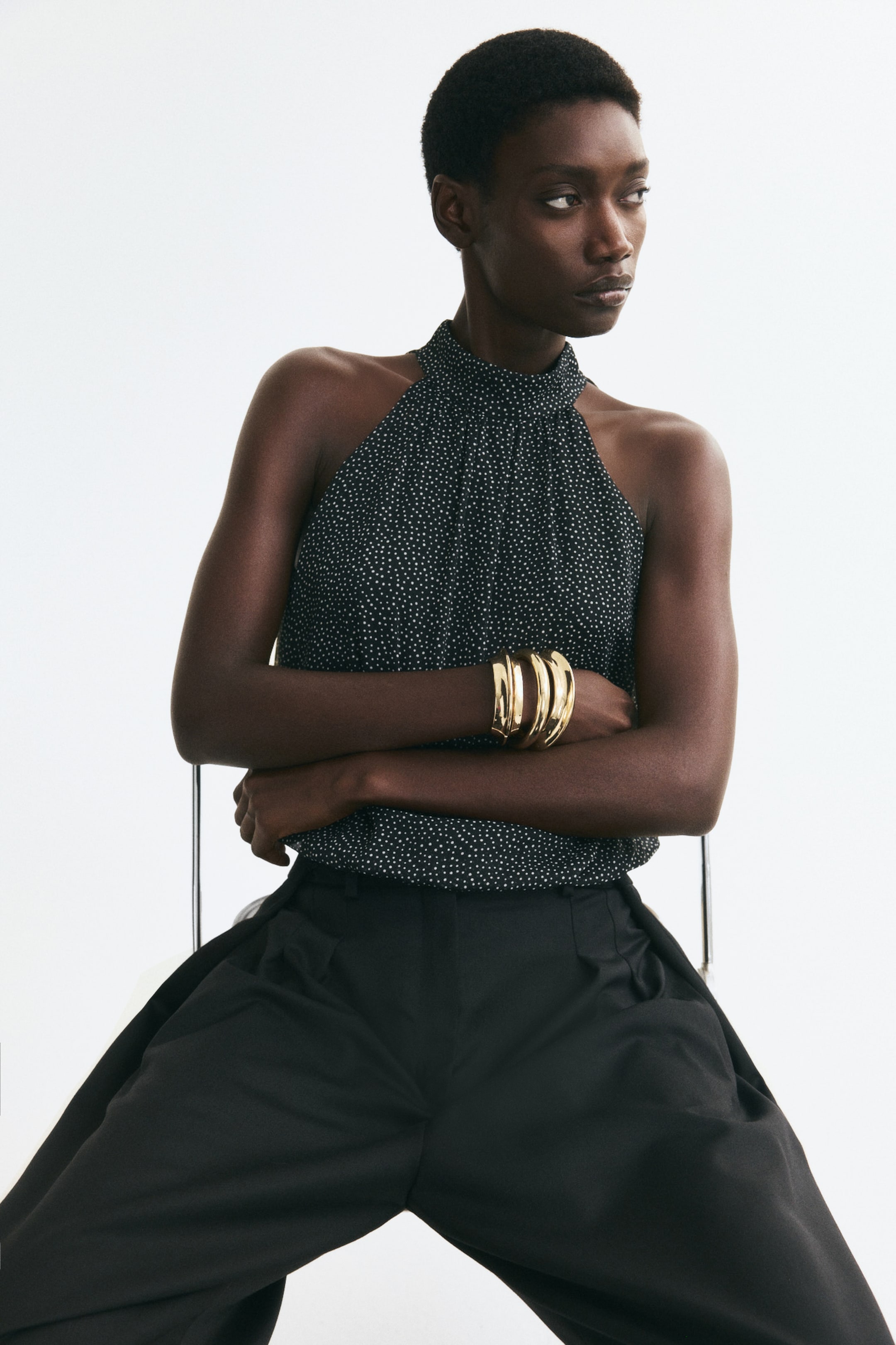 Agrandir l'image: Un haut dos-nu sans manches à pois noirs et blancs est porté par le mannequin. Le haut présente un col montant et une coupe étroite aux épaules, associé à un pantalon noir à jambes larges.