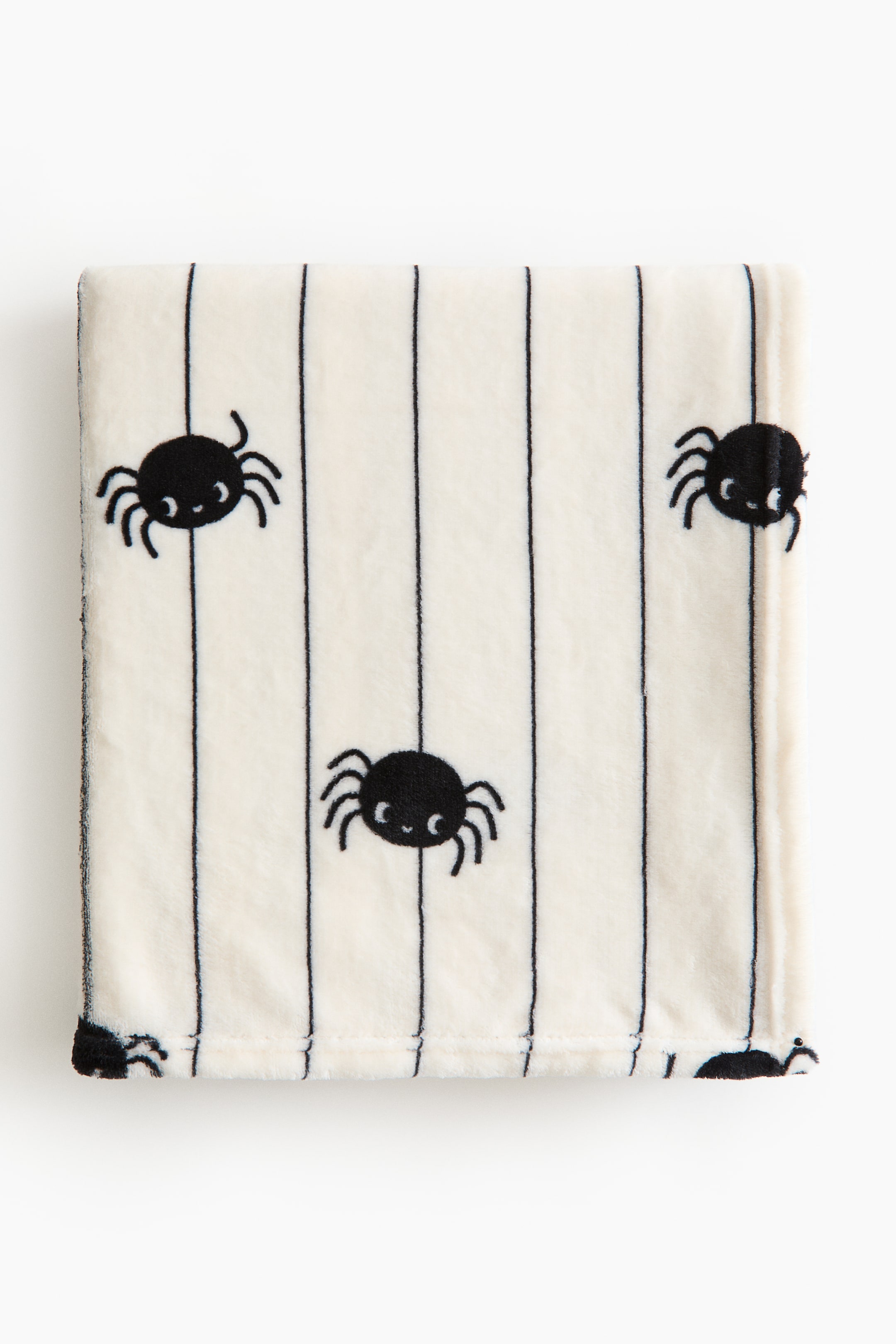 View larger image: A soft fleece blanket features a cream base color and a pattern of black vertical stripes and black cartoon spiders with white eyes. It is presented folded flat.