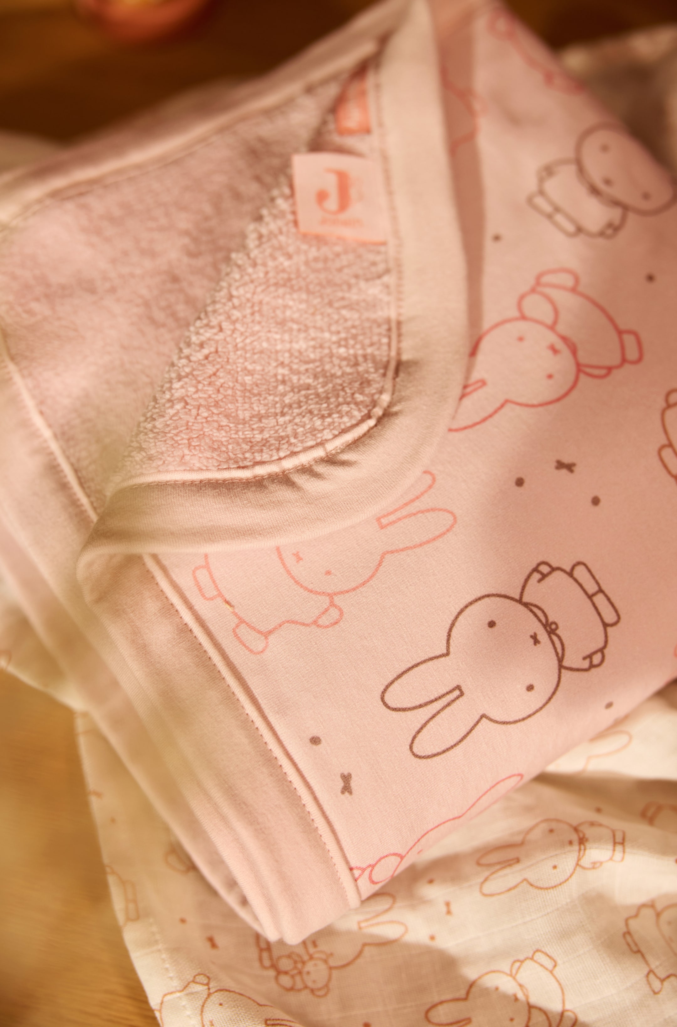 Agrandir l'image: Une couverture pour bébé rose pliée présente, sur son envers lisse, un motif répété de contours de lapins de dessin animé. Le coin est replié, révélant un revers en tissu éponge rose texturé et une bordure en tissu rose uni le long des bords.