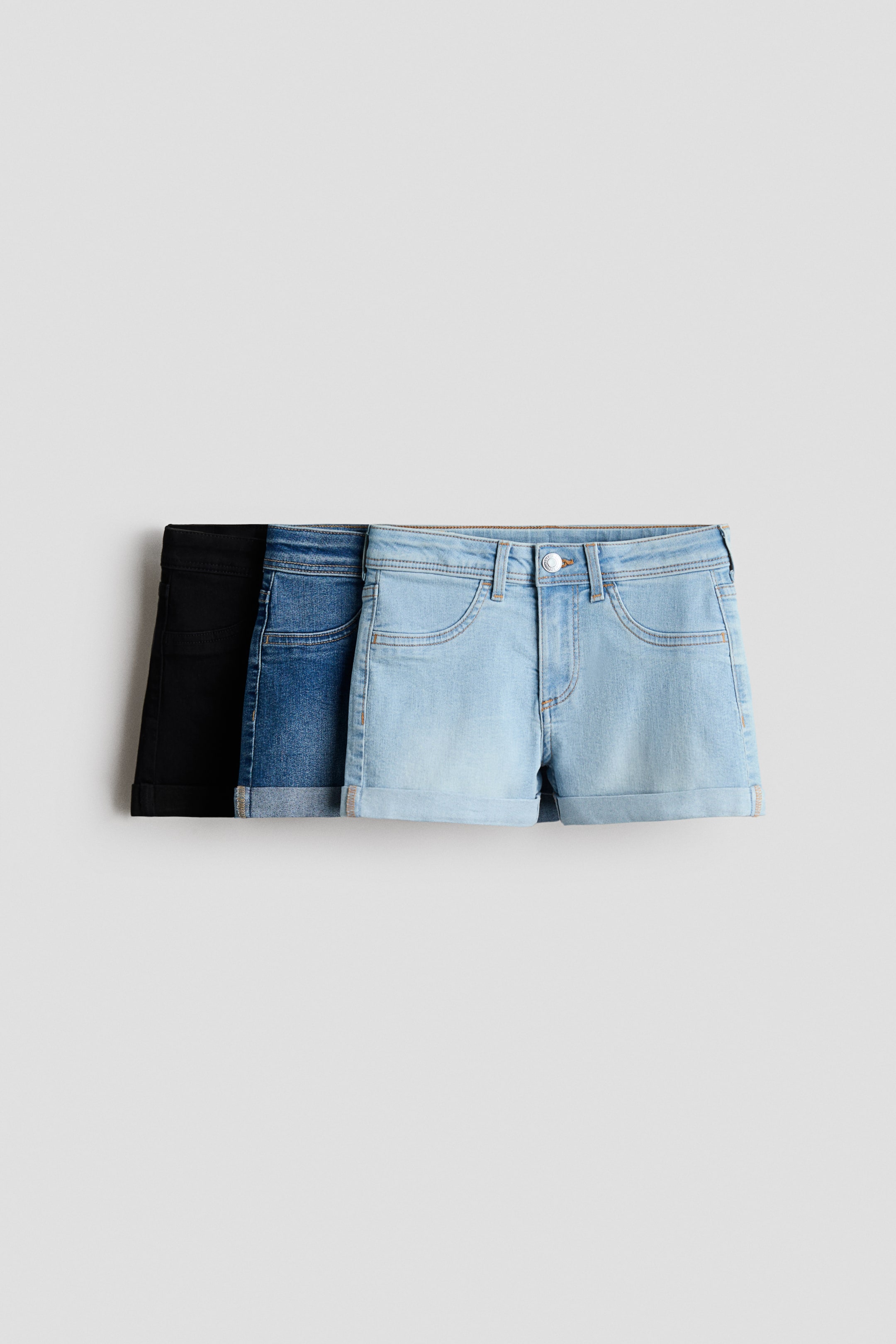 Agrandir l'image: Trois paires de shorts en jean slim-fit sont exposées de face, superposées du bleu clair au bleu moyen au noir. Chaque paire est dotée d'une fermeture éclair avec bouton, de fausses poches avant et de revers cousus aux ourlets.