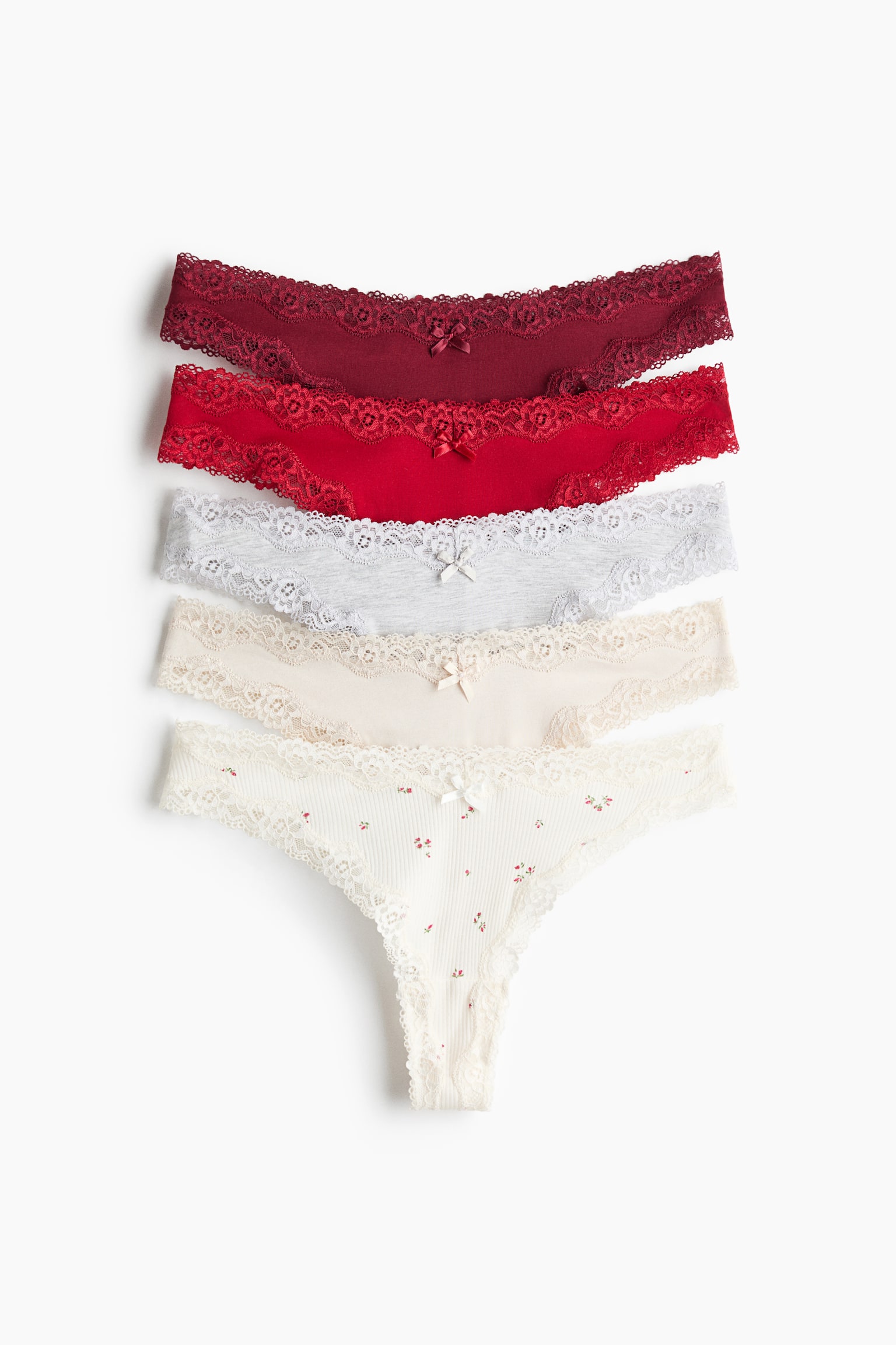 Five pairs of cotton jersey and lace briefs are displayed in a vertical stack from the front, featuring a mid-rise fit with a V-shaped waist, lace-trimmed edges, and a small bow at the center. The collection showcases a range of colors from top to bottom, including burgundy, red, heather gray, cream, and an off-white pair patterned with small red flowers.