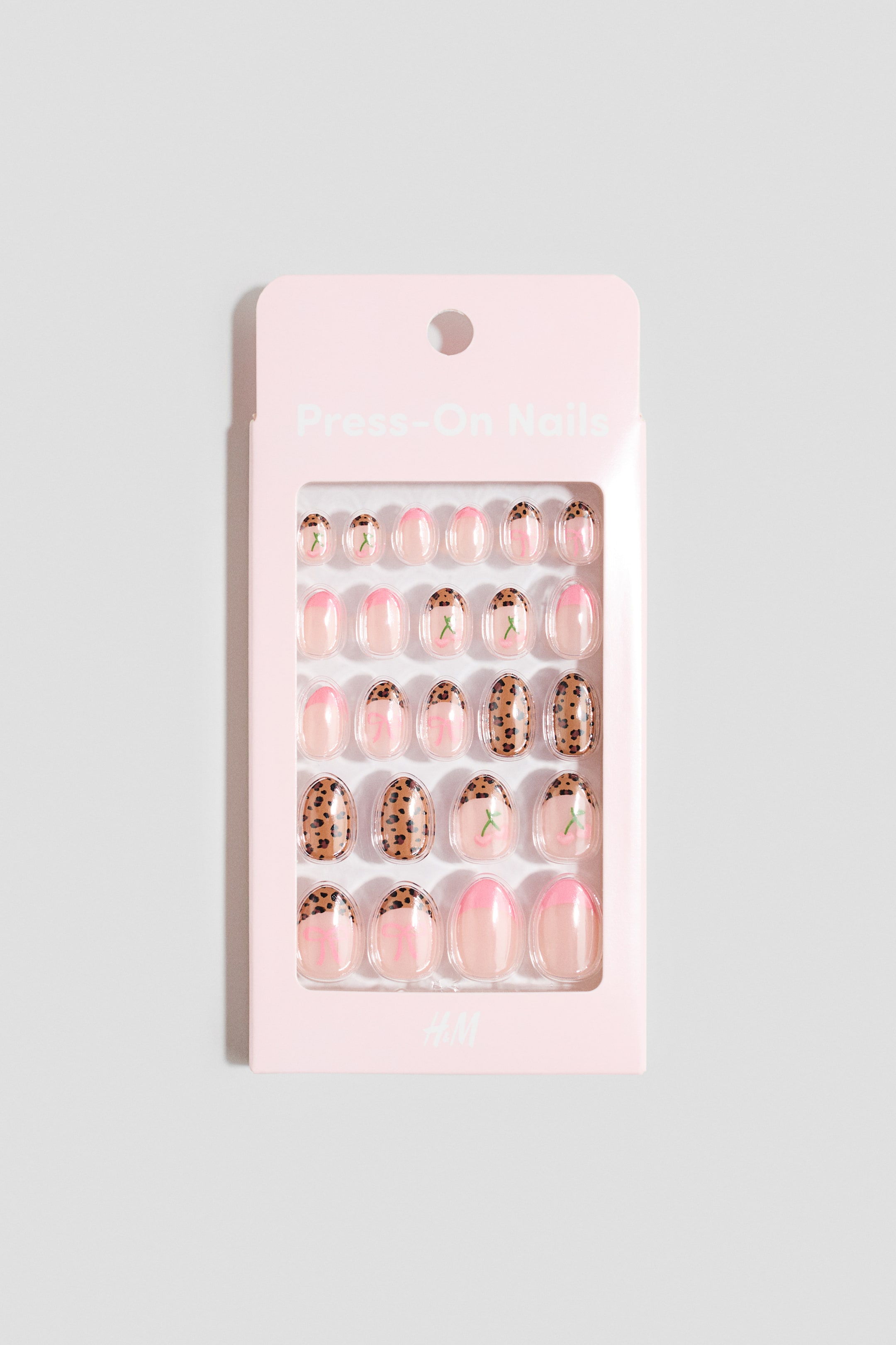 Größeres Bild ansehen: Ein rosa rechteckiges Paket zeigt 24 aufklebbare Nägel, die in Reihen angeordnet und nach vorne ausgerichtet sind. Die Nägel haben eine natürliche rosa Basis mit Designs, darunter rosa French Tips, braun-schwarzer Leopardenprint, grüne Stiele, rosa Schleifen und rosa Kirschen.