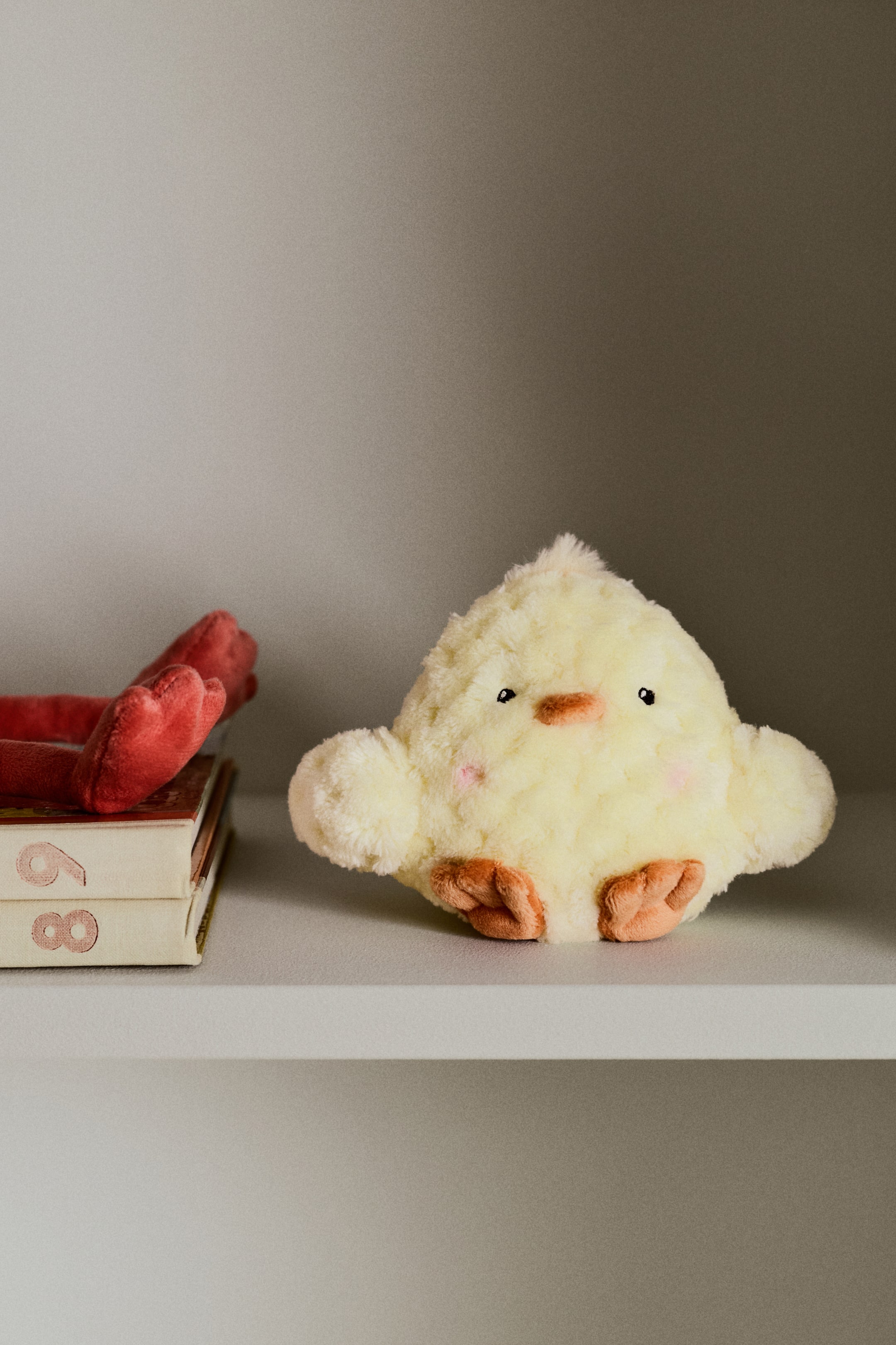 Visualizza immagine più grande: Un peluche a forma di pollo è rivolto FRONTE, caratterizzato da un morbido piumaggio giallo. Presenta un corpo rotondo e abbracciabile con piccoli piedi marroni, un becco marrone, occhi neri e segni di rossore rosa sulle guance.