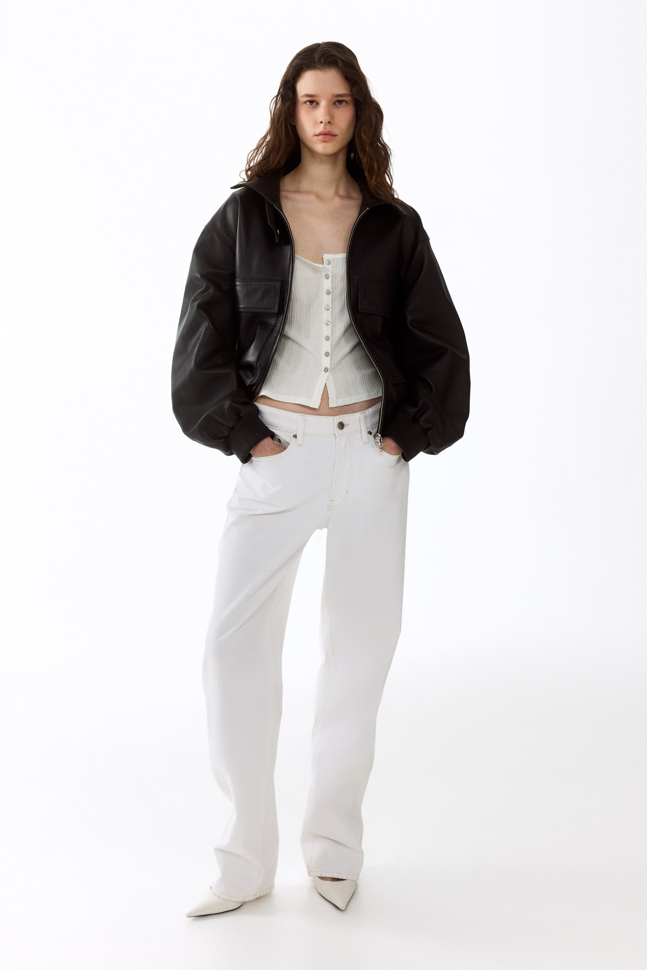 View larger image: The black leather bomber jacket showcases an oversized fit, styled with the front zipper open over a white ribbed top. It features a stand collar, two chest flap pockets, and ribbed cuffs and hem, perfect for a chic and contemporary look.