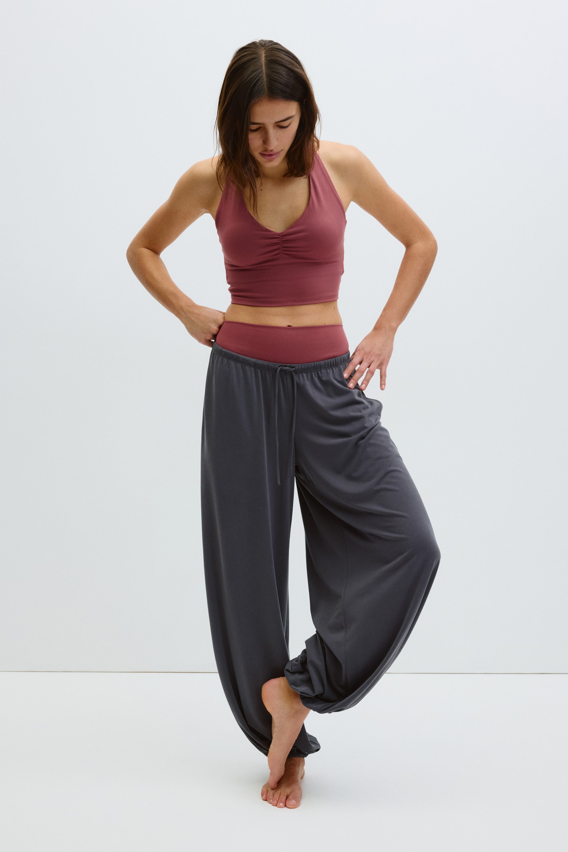 Ver imagen más grande: Los pantalones harem gris oscuro presentan un ajuste holgado y voluminoso con una entrepierna caída, y se estrechan hacia los tobillos recogidos. Un cordón gris oscuro es visible en la parte frontal de la cintura elástica.