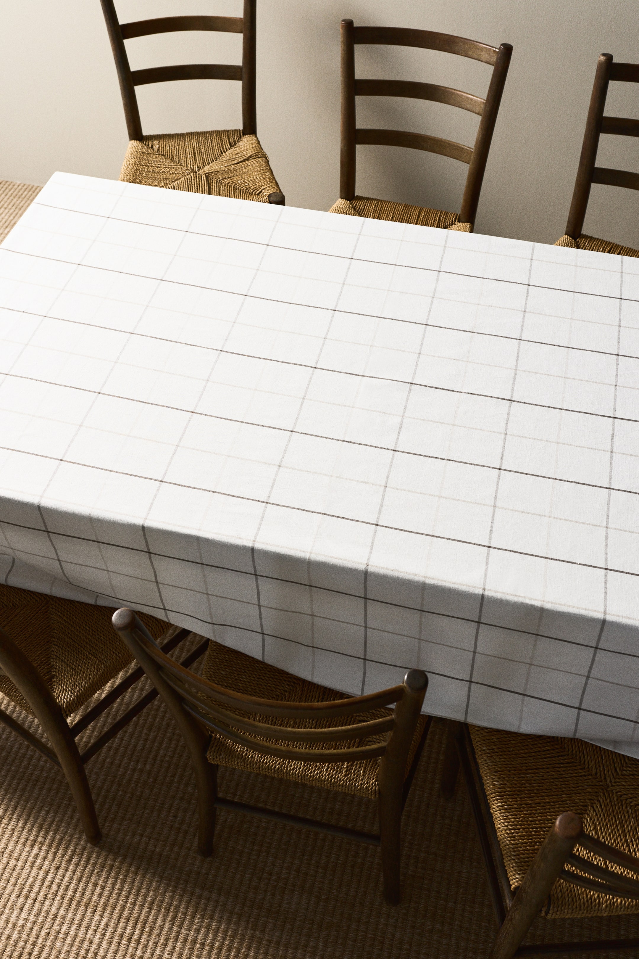Voir une image plus grande: Une nappe blanche recouvre une table, arborant un motif subtil de grille composé de fines lignes gris foncé et gris clair. Elle tombe élégamment sur les bords de la table, mettant en valeur sa texture et son design d'une perspective en plongée.