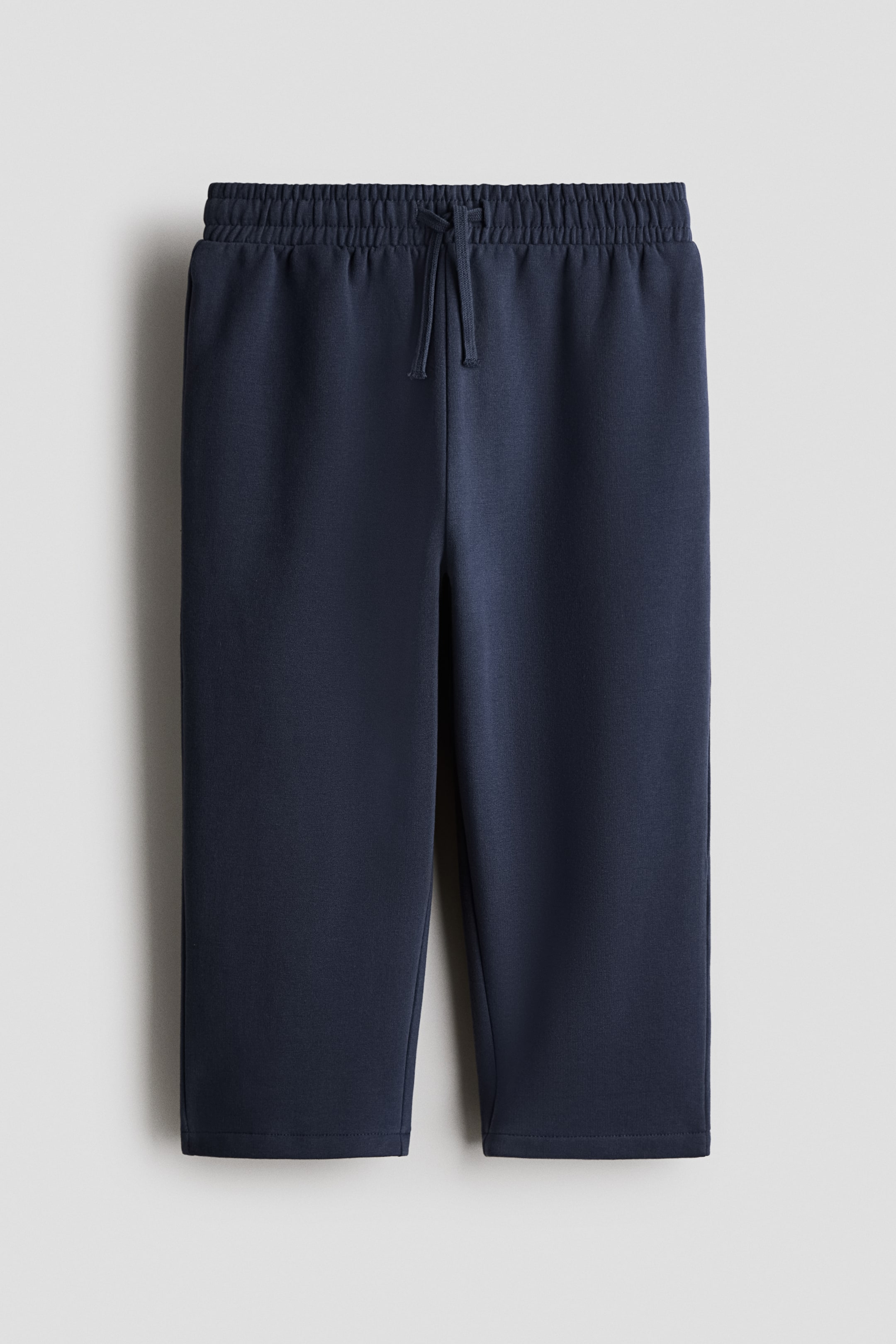 Se større billede: Mørkeblå joggers har en elastisk snørelukning i taljen foran. De er designet med lige ben og et glat, sweatshirt-agtigt stof.