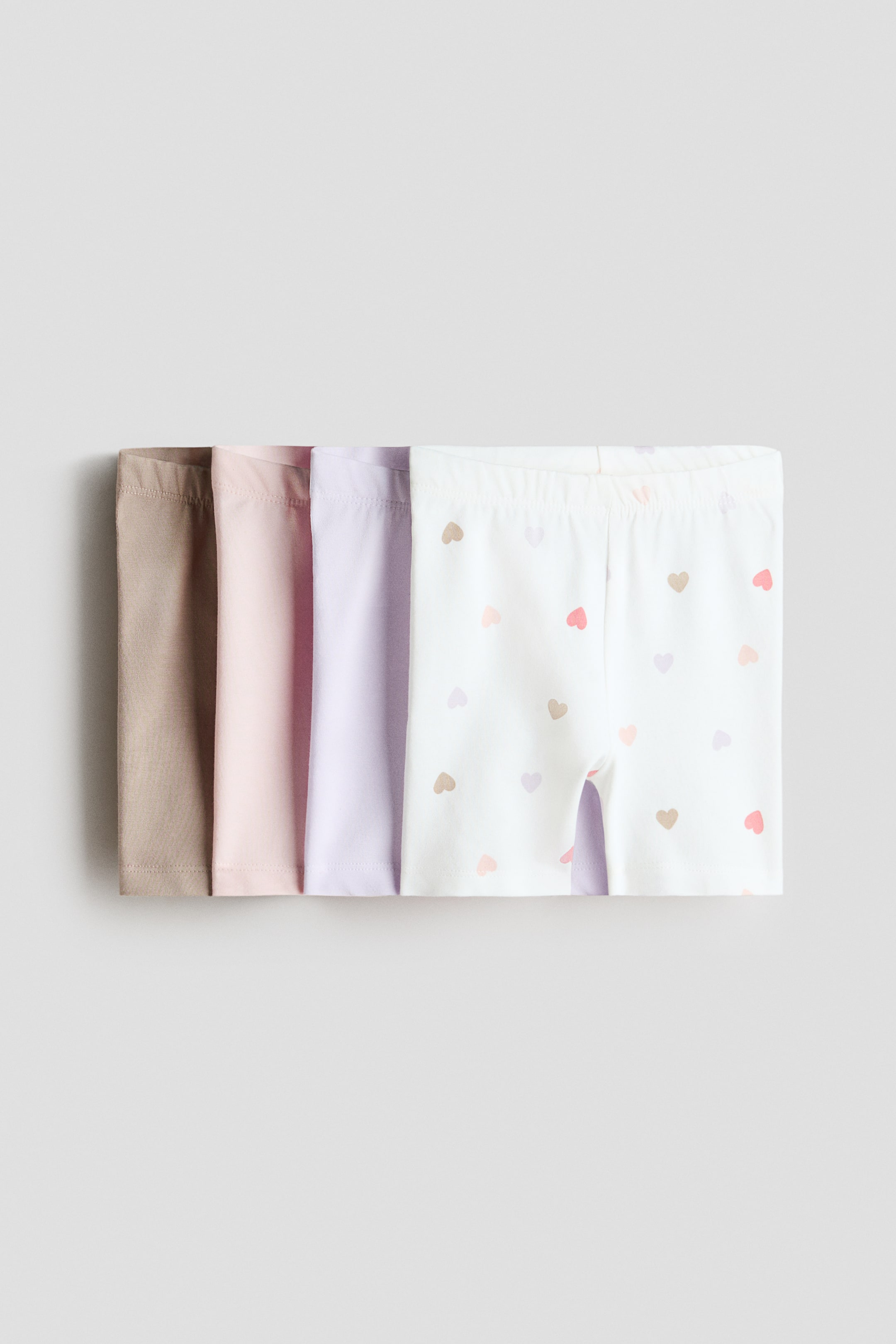 Agrandir l'image: Shorts de cyclisme en jersey de coton doux avec taille élastiquée, présentés en pile de quatre paires. La paire du dessus, vue de face, est blanche avec des motifs de cœurs pastel épars, et les paires partiellement visibles en dessous sont de couleur unie marron clair, rose clair et violet clair.