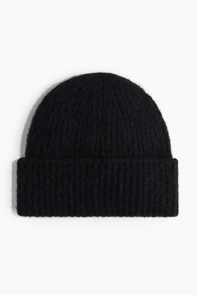 A black beanie is featuring a wide, ribbed cuff, while its crown is displaying a smoother knit with a slightly fuzzy texture. - 1