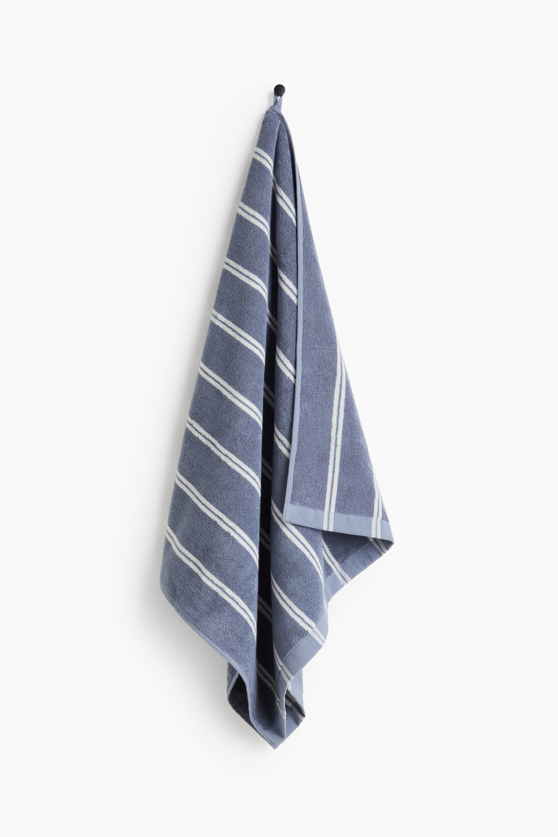 View larger image: "A blue terry bath towel is hanging, showcasing white diagonal stripes, a woven hem, and a visible hanger loop at the top."