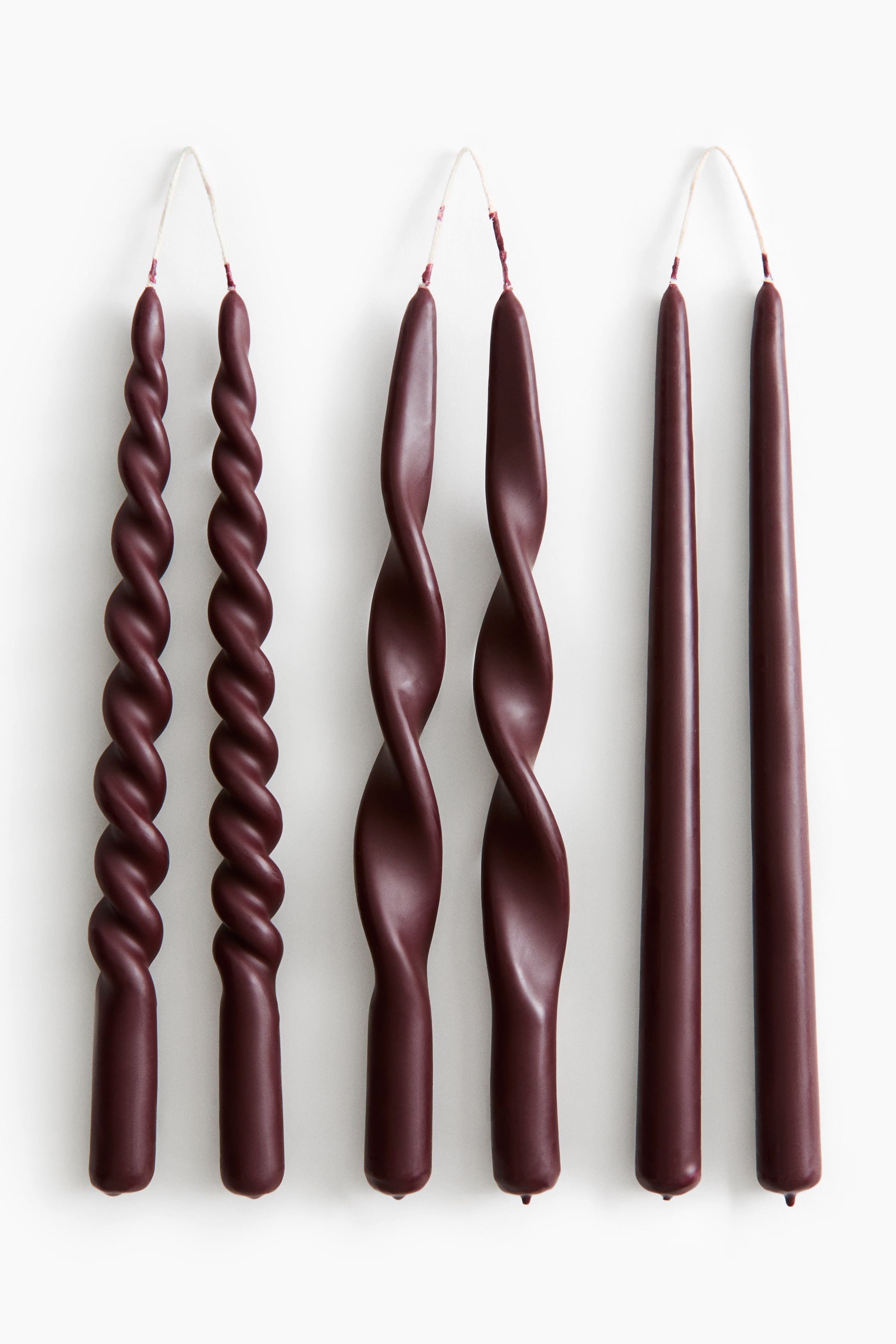 Agrandir l'image: Trois paires de bougies effilées bordeaux foncé sont disposées de face, chaque paire étant reliée en haut par une mèche claire continue. Les bougies présentent trois motifs distincts : une spirale serrée à gauche, une spirale lâche au centre et une forme effilée classique et lisse à droite.
