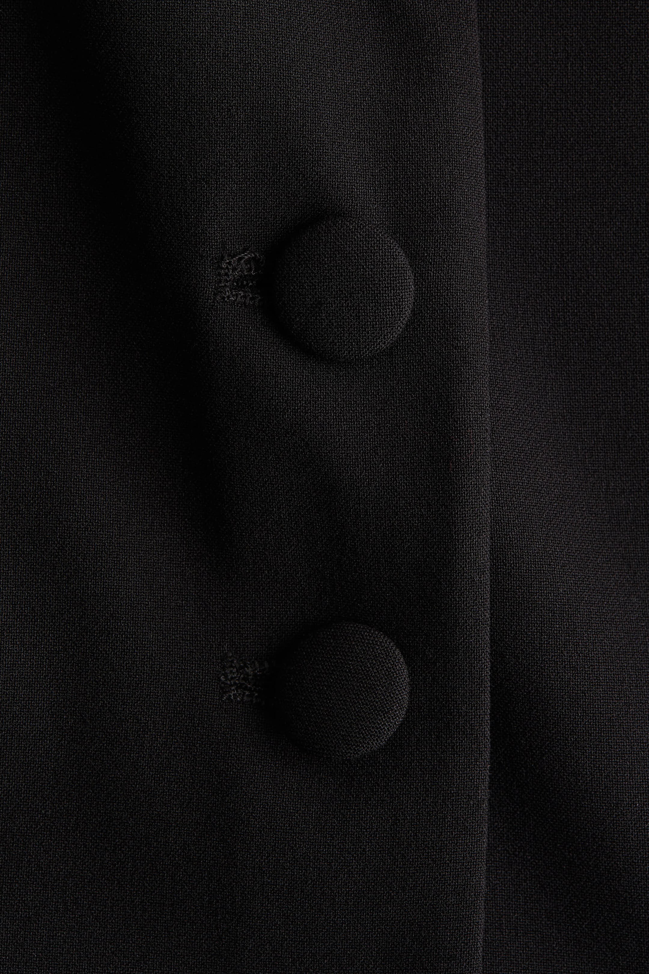Agrandir l'image: Un haut ajusté à manches courtes présente une vue rapprochée de son tissu tissé noir. Deux boutons recouverts de noir sont alignés verticalement sur le DEVANT du vêtement, avec une couture de forme subtile visible à côté d'eux.