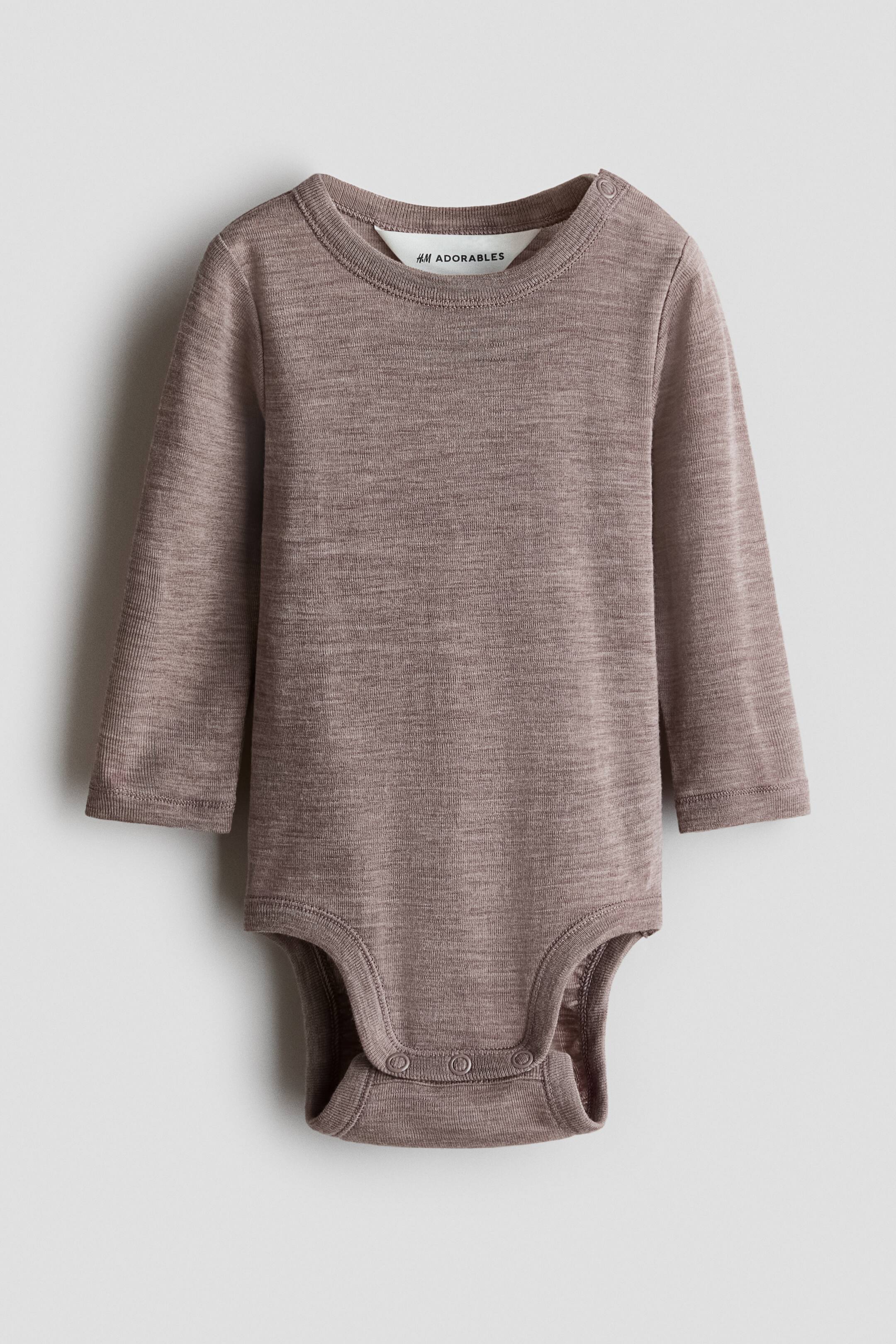 Grösseres Bild ansehen: Ein meliert brauner Strick-Baby-Body wird flach liegend und von vorne präsentiert. Er verfügt über einen Rundhalsausschnitt mit zwei Druckknöpfen an der linken Schulter, lange Ärmel mit genähten Bündchen und drei Druckknöpfen im Schrittbereich.