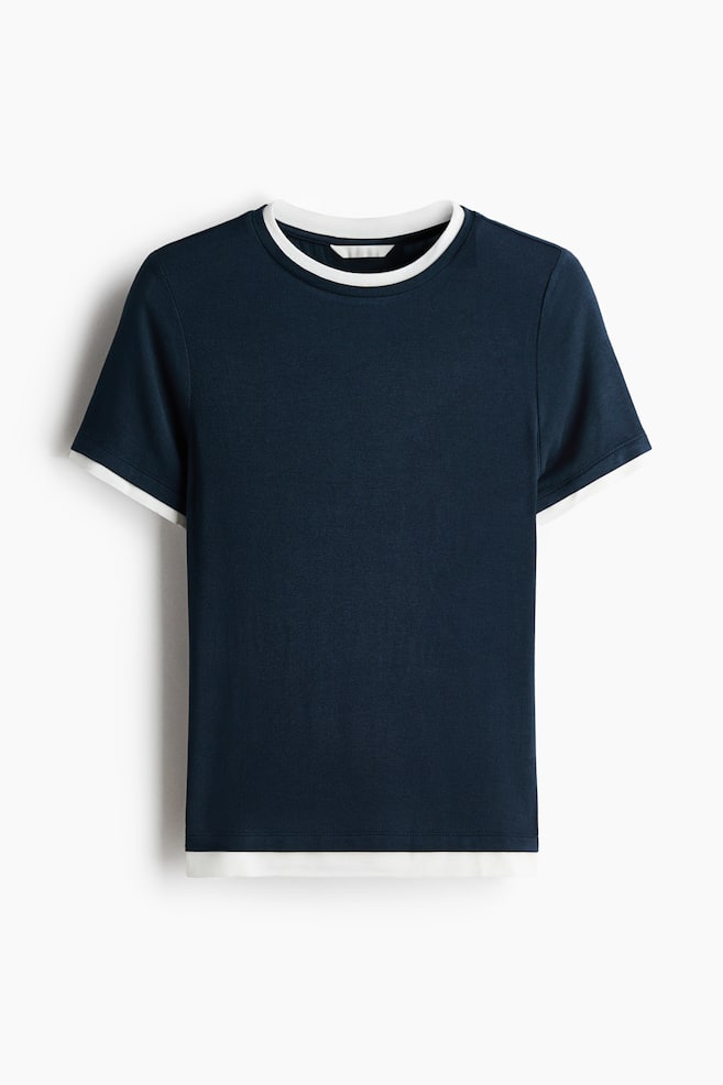 A navy blue t-shirt is presented flat, featuring a white trim around the crew neck and sleeve openings. A white layer is also visible extending from the bottom hem, creating a layered appearance. - 1