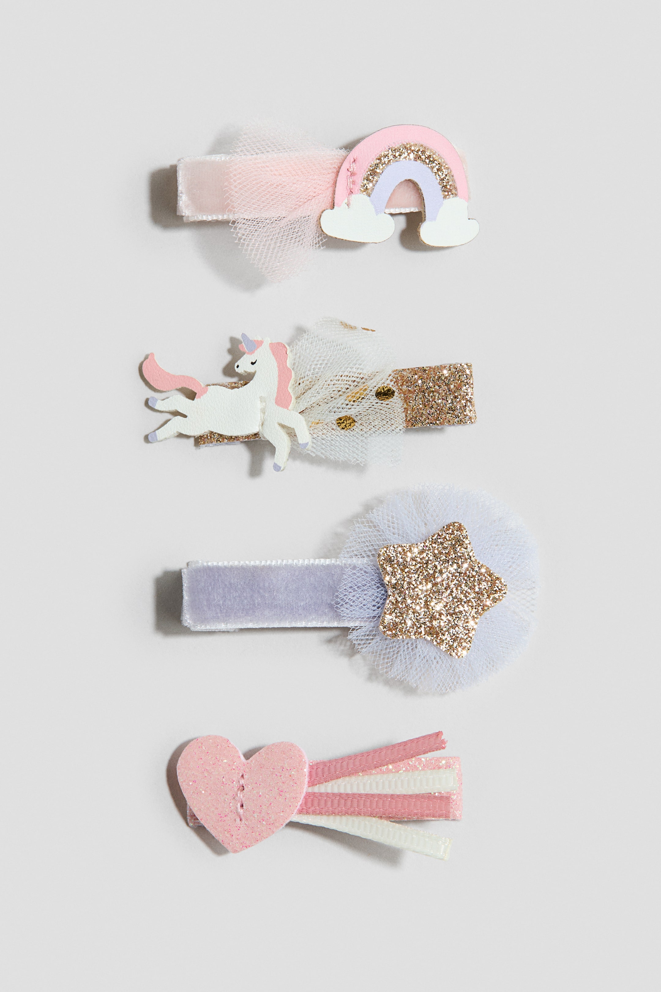 Visa större bild: 4-pack hårklämmor visas från framsidan, var och en med en unik design. Klämmorna visar en rosa sammetklämma med en pastellregnbåge och rosa tyll, en guldglitterklämma med en vit enhörning och vit prickig tyll, en ljuslila sammetklämma med en guldglitterstjärna och vit tyll, samt en glittrig rosa hjärtklämma med rosa, vita och glittriga bandströmmar.