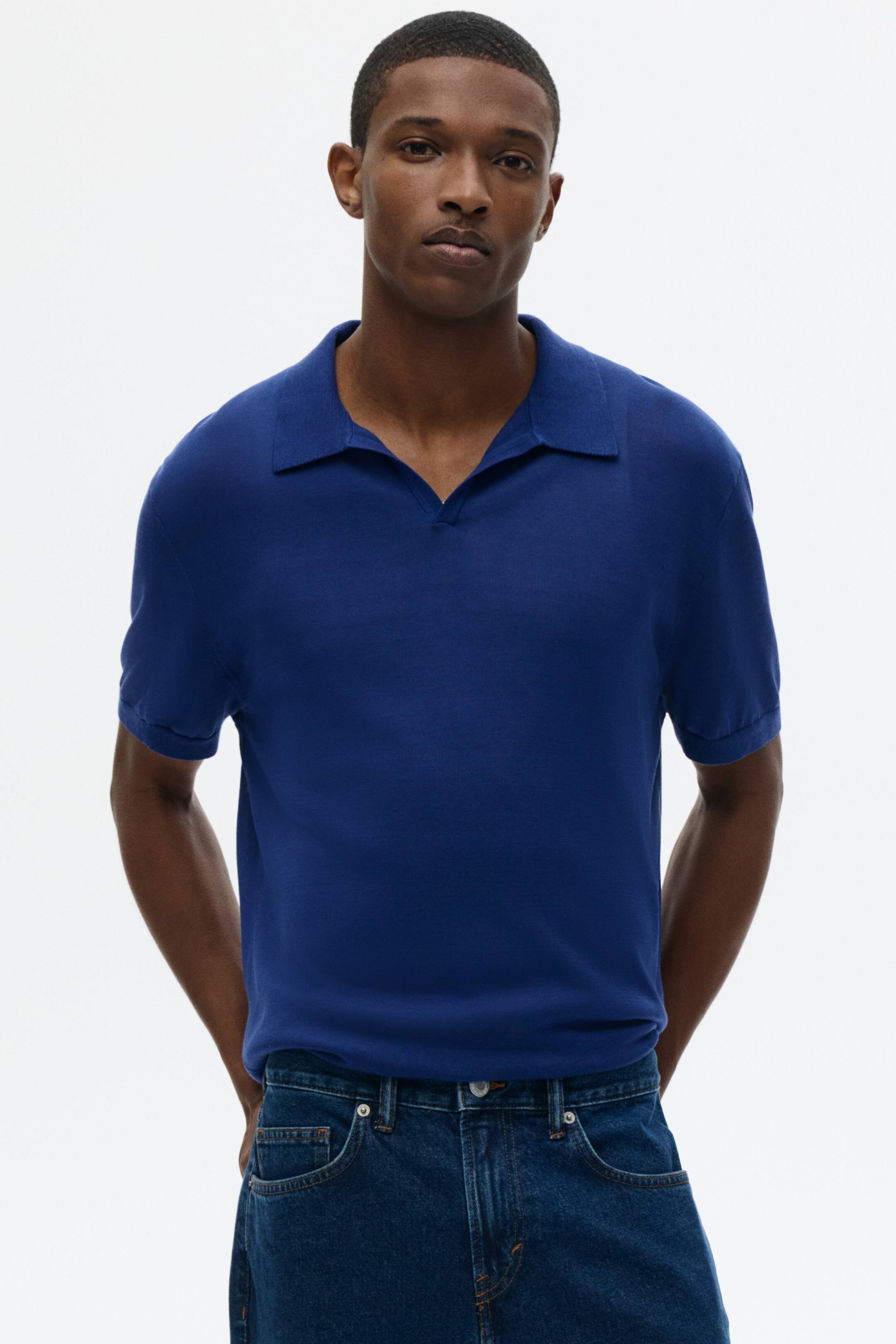 View larger image: A royal blue knit polo shirt features a spread collar and an open V-neck placket. It is designed with short sleeves finished with simple hems.