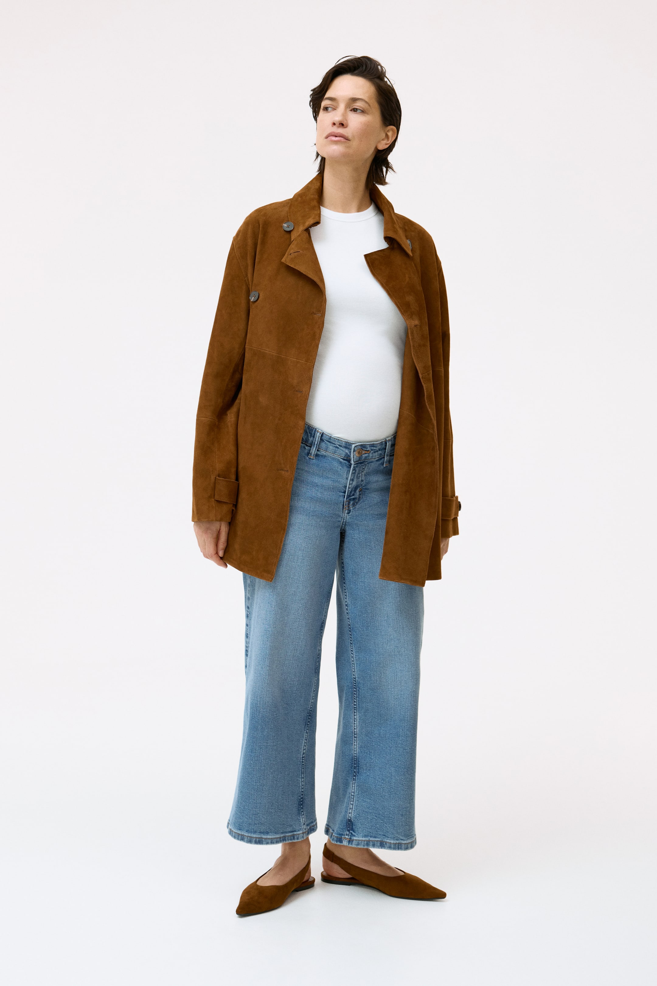 View larger image: The brown suede jacket features a double-breasted design with notch lapels and buttoned cuff tabs. Styled open, it reveals a white t-shirt underneath and offers a relaxed fit.