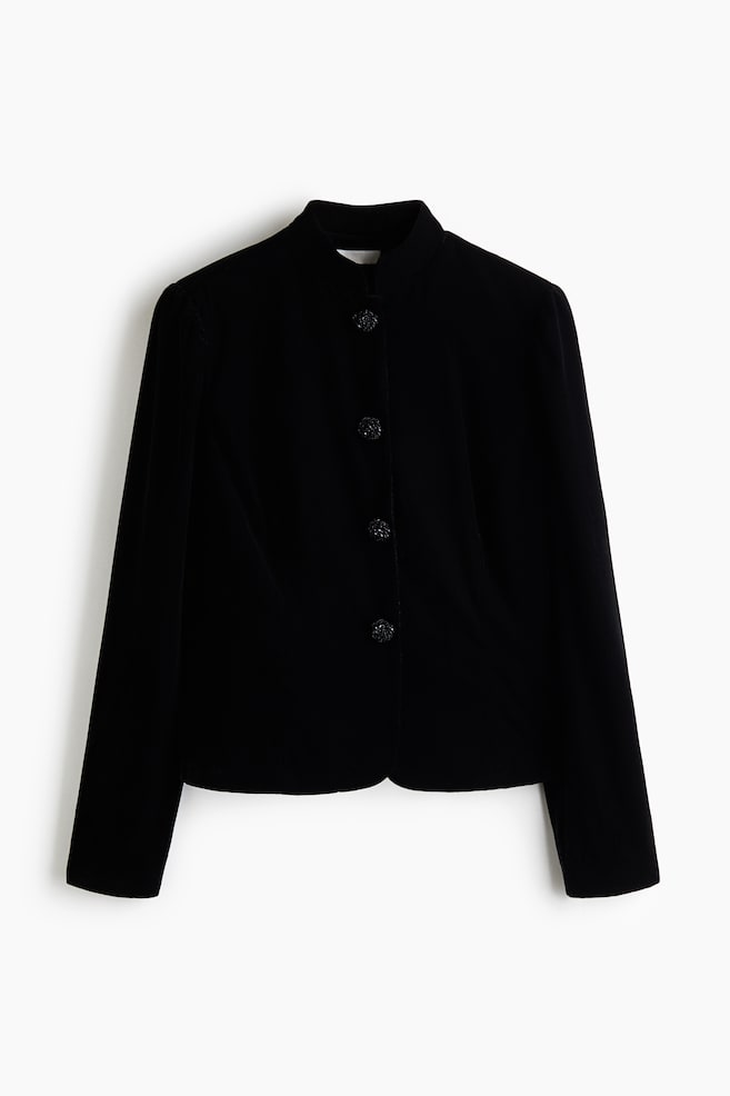 A black velvet jacket is shown from a front-facing perspective, featuring a structured stand collar, long sleeves, and a straight hem. The jacket fastens down the centre front with four large, textured black buttons. - 1