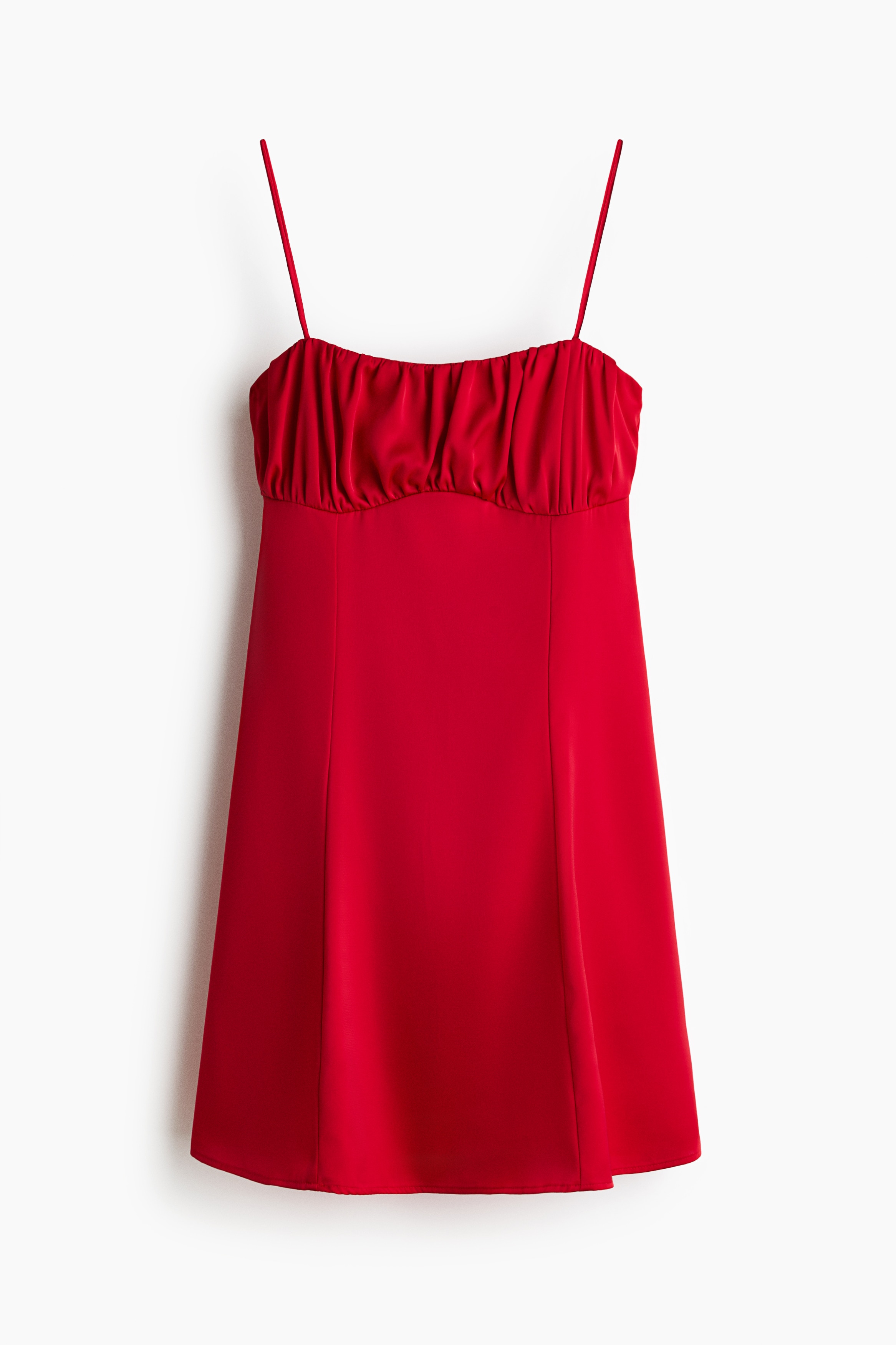 A model is wearing a short, bright red dress in a front-facing view, featuring a straight neckline with a gathered, ruched bust and thin spaghetti straps. The dress has visible vertical seams running down the front of its gently flared skirt and is styled with an oversized black leather jacket and off-white sneakers.