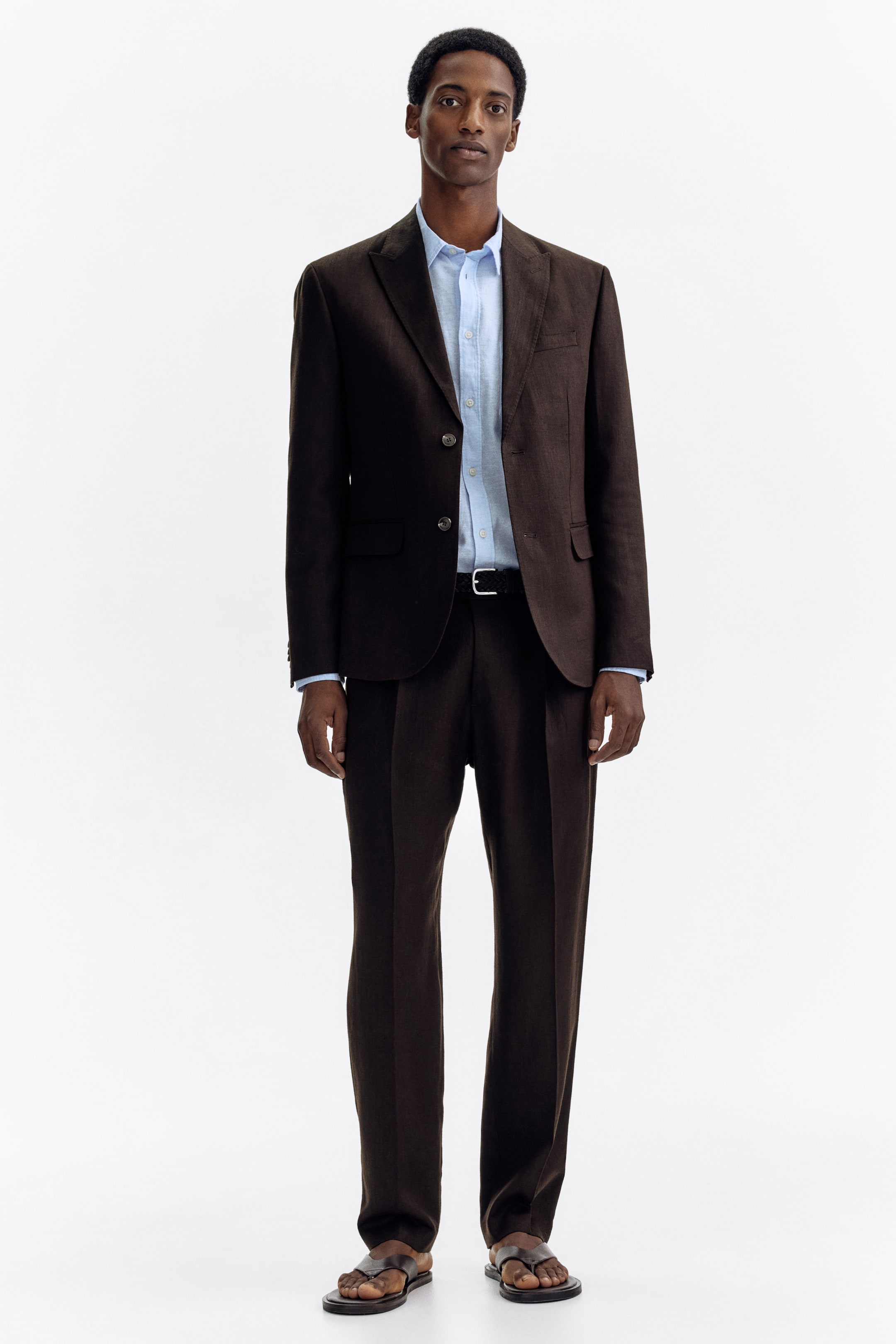 View larger image: A dark brown textured suit is showcased, facing forward. The jacket boasts notch lapels, a two-button closure, a chest welt pocket, and two flap pockets, while the matching straight-leg trousers feature front creases. A light blue shirt and a black belt accompany the suit.