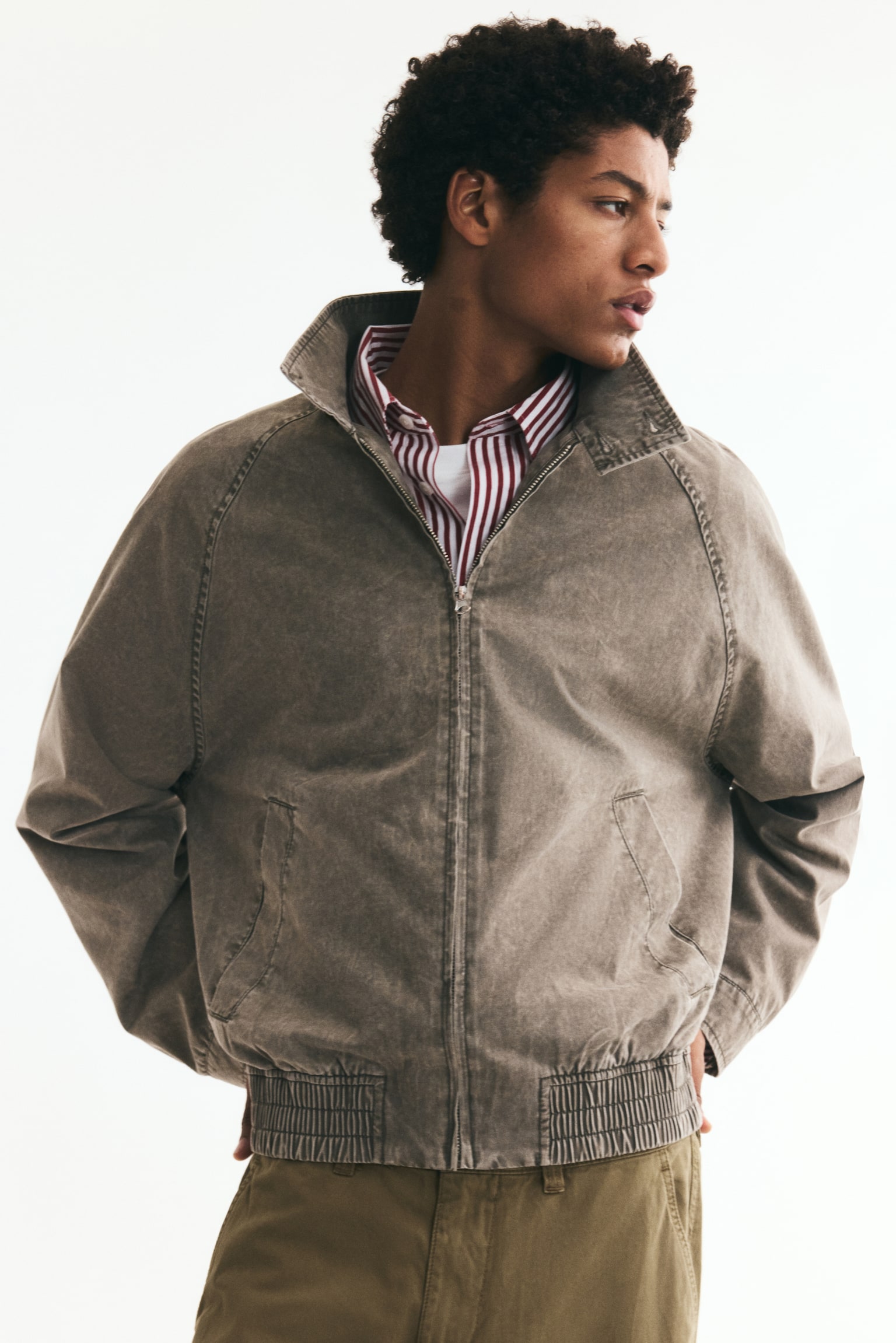 A stone-washed brown jacket is displaying its front, featuring a stand-up collar with a snap button, a central zipper closure, raglan sleeves, two slanted welt pockets, and a ribbed elasticated hem. - 1