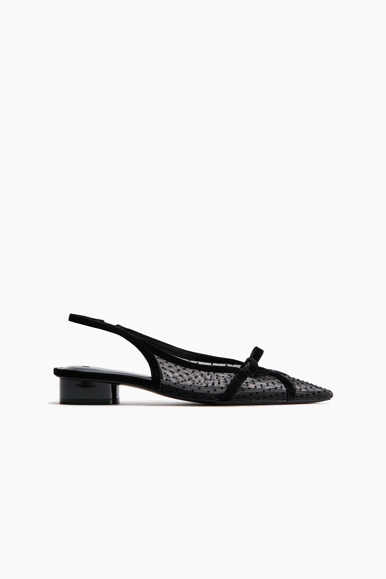 Une chaussure slingback noire est prÃ©sentÃ©e de profil, avec un bout pointu et une tige en maille transparente dÃ©corÃ©e de petits pois. La chaussure affiche un talon bloc bas et brillant, une fine bride slingback et un dÃ©licat nÅud noir sur lâempeigne.