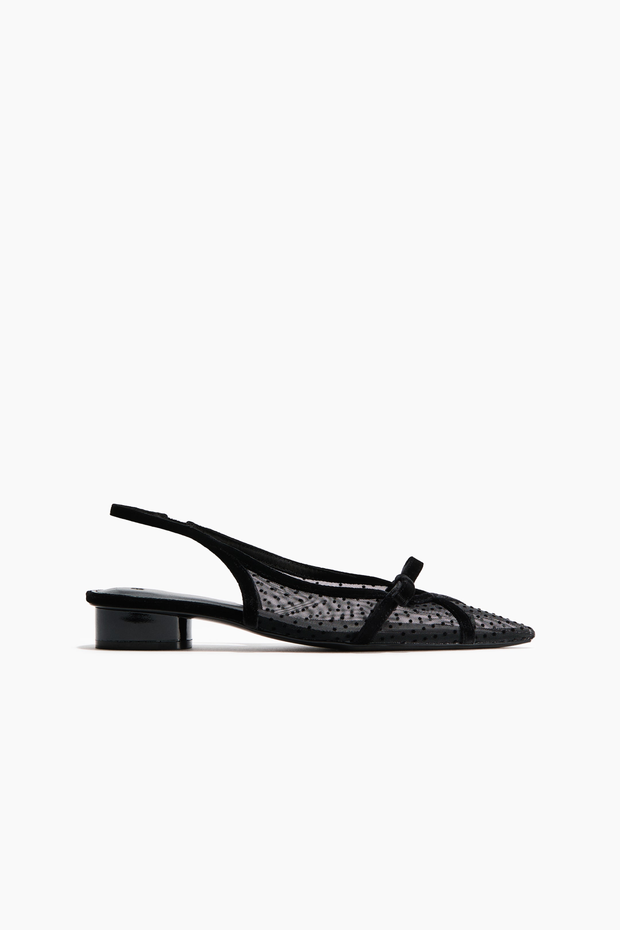 Ver imagen más grande: Se muestra un zapato slingback negro en vista lateral, con puntera afilada y un empeine de malla translúcida decorado con pequeños lunares. El zapato presenta un tacón bajo y brillante de bloque, una fina tira slingback y un delicado lazo negro sobre el empeine.