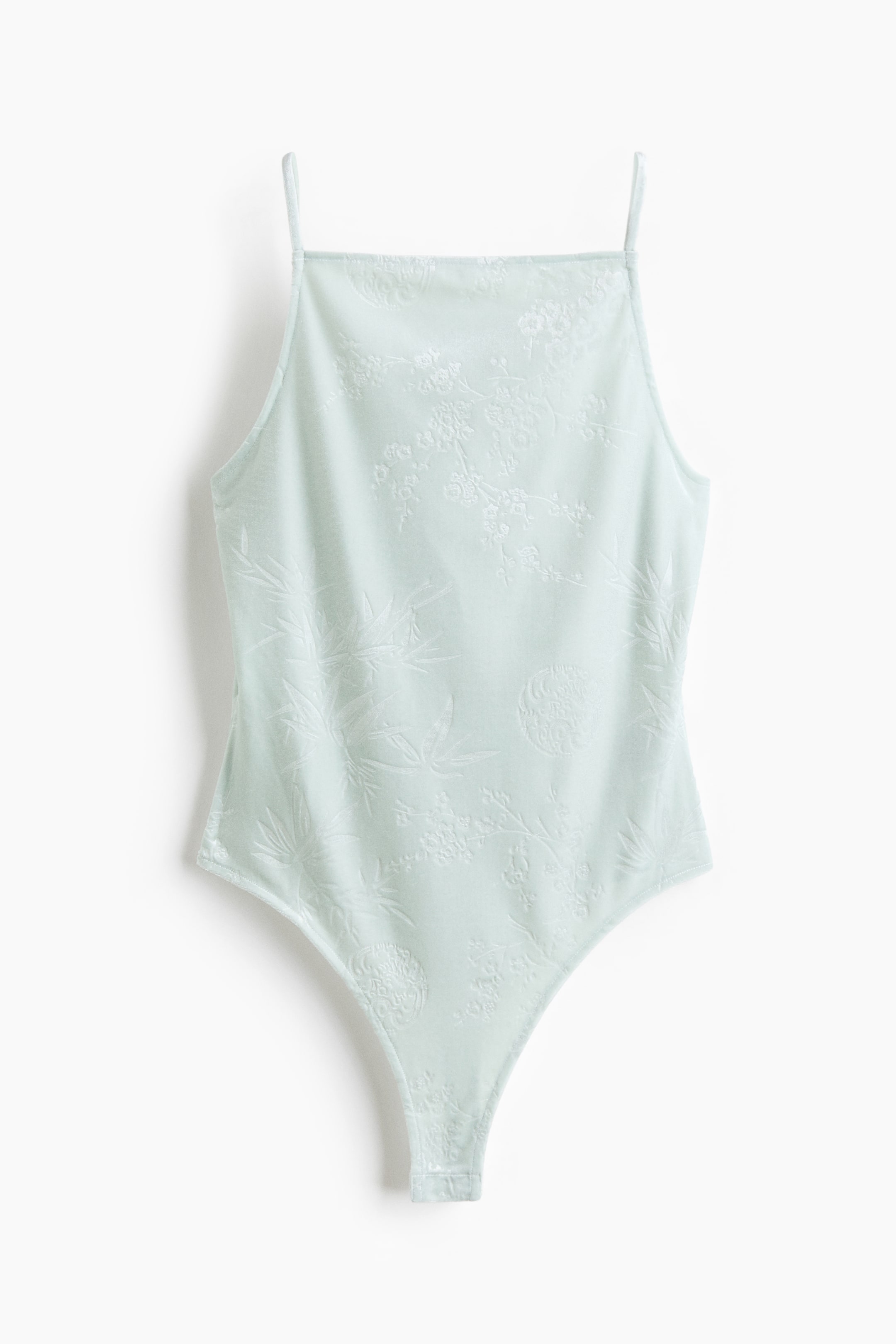 View larger image: A light mint green bodysuit is shown from the front, featuring a square neckline and thin spaghetti straps. The fabric displays a subtle, tone-on-tone jacquard pattern with floral and bamboo leaf designs, tapering down to a high-cut leg opening.