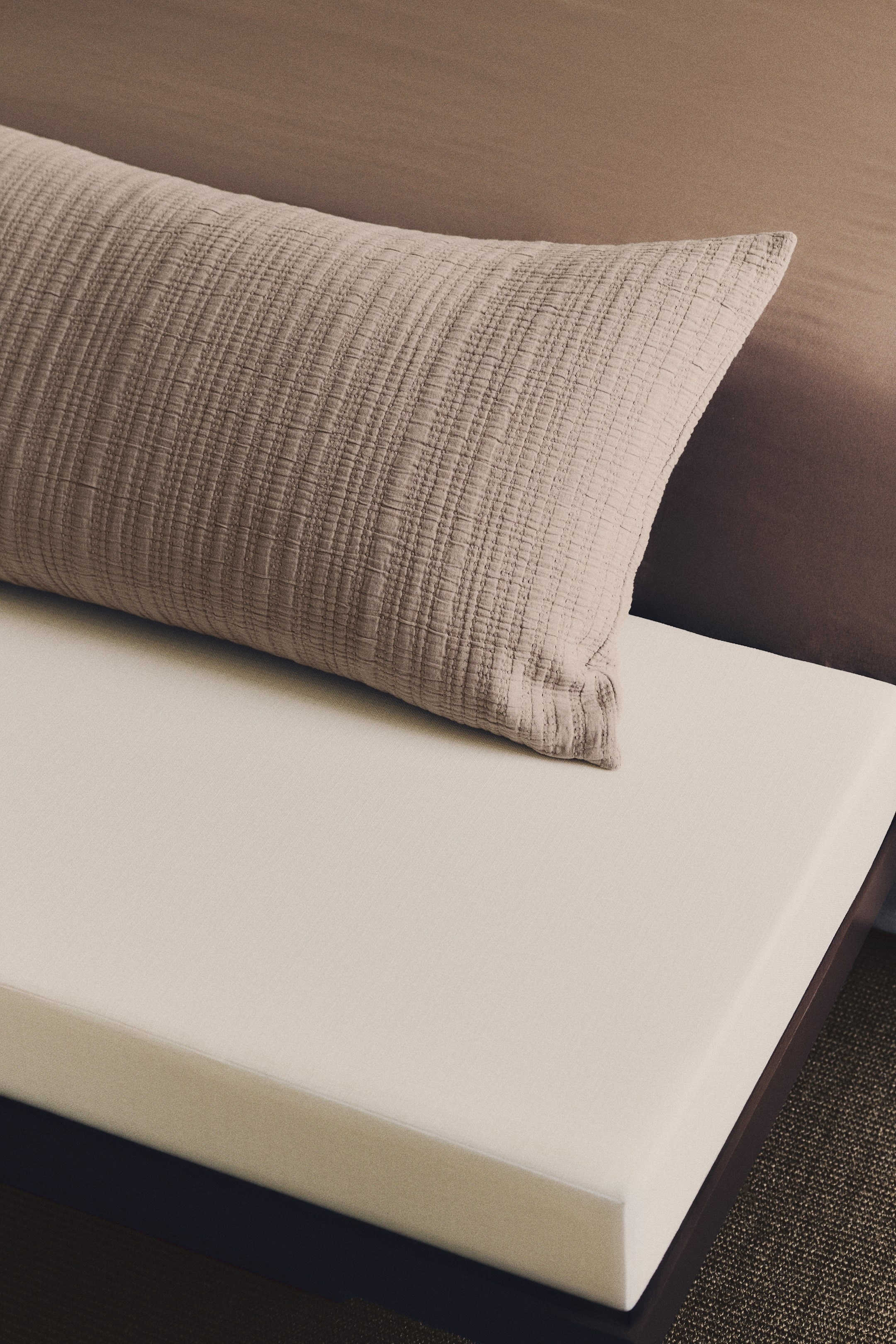 View larger image: A light beige rectangular cushion, featuring a textured quilted pattern, is resting at an angle on a smooth, off-white rectangular seat cushion.